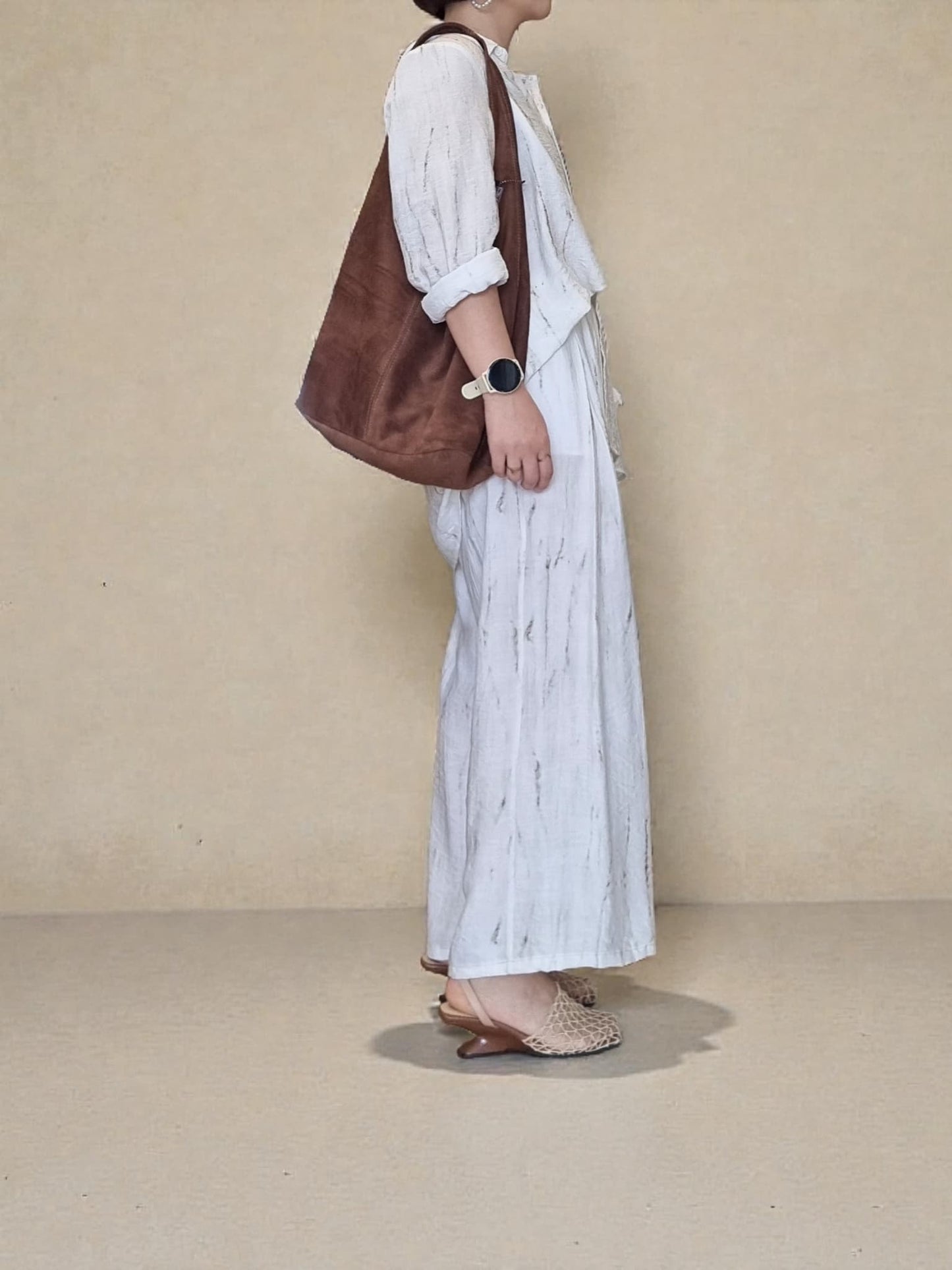 “Side view of a model carrying a brown suede shoulder bag, highlighted against a beige background.”