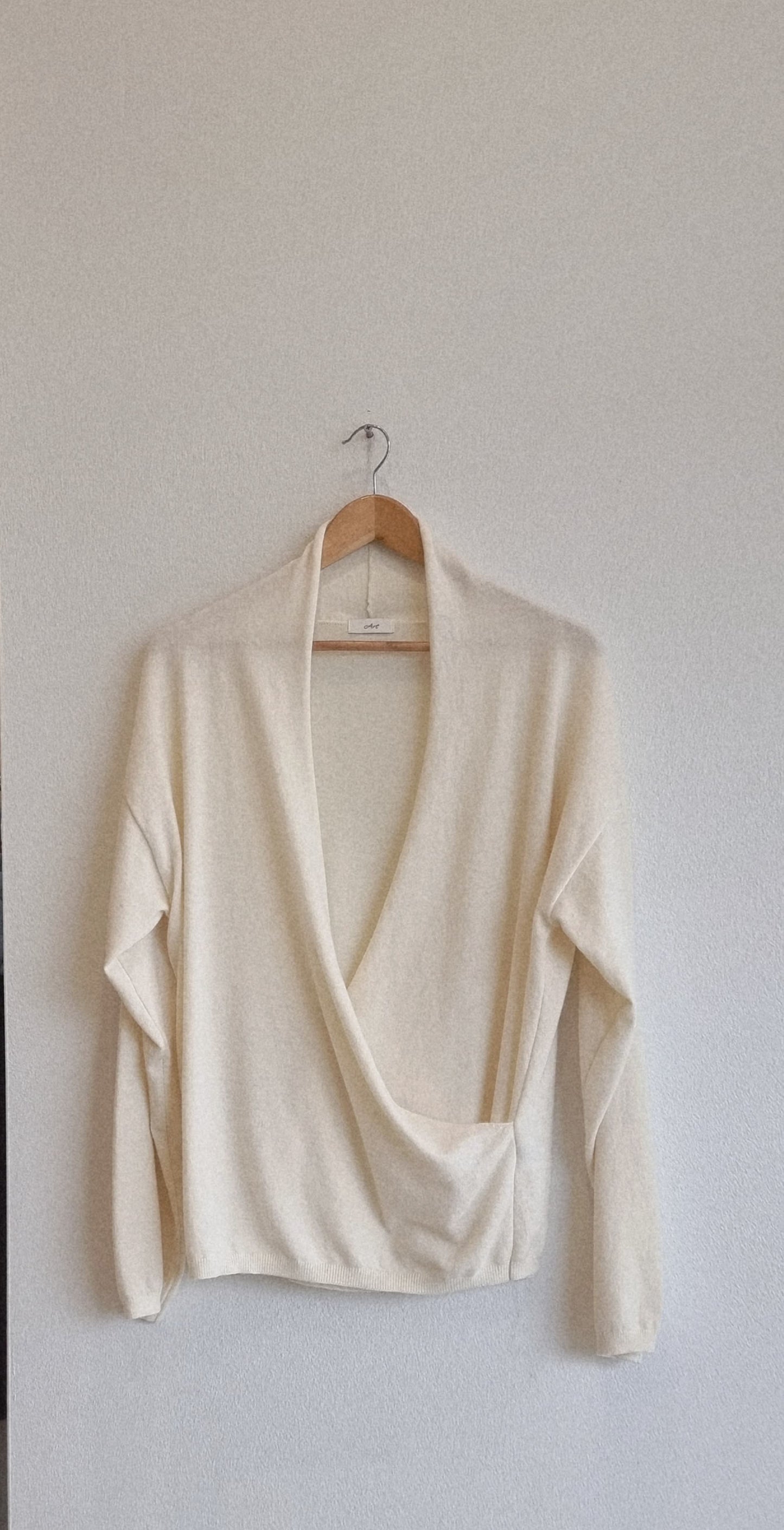 Cream wrap knit top hanging on hanger, product only