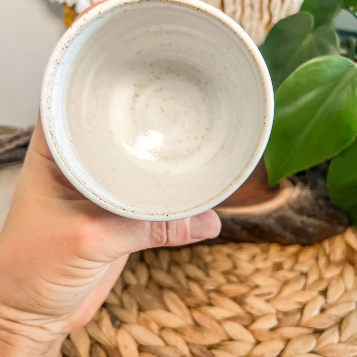 “Top view of a handmade ceramic mug showing the speckled interior, held in one hand.”