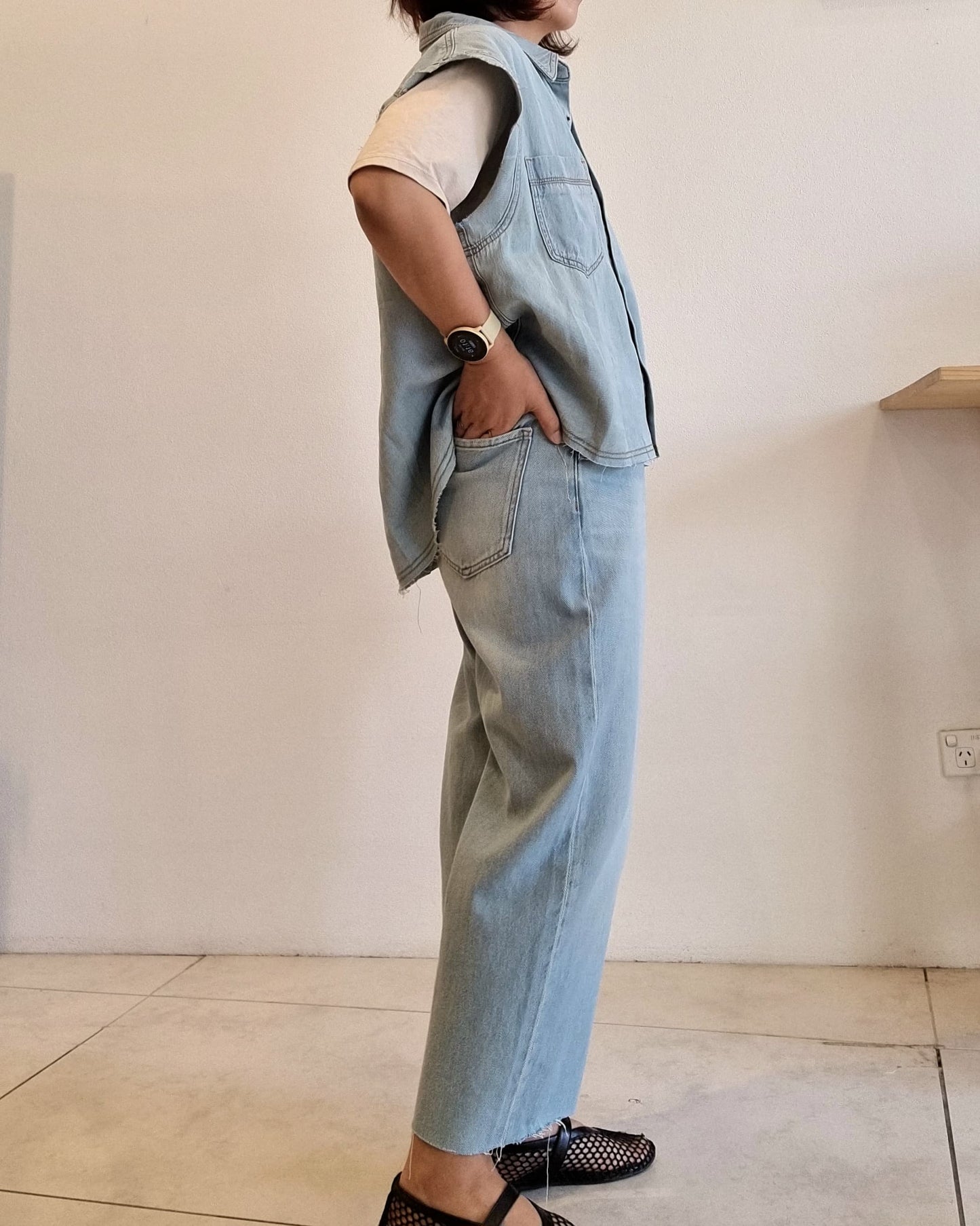 Light denim cotton vest, angled back-side view showing hem detail.