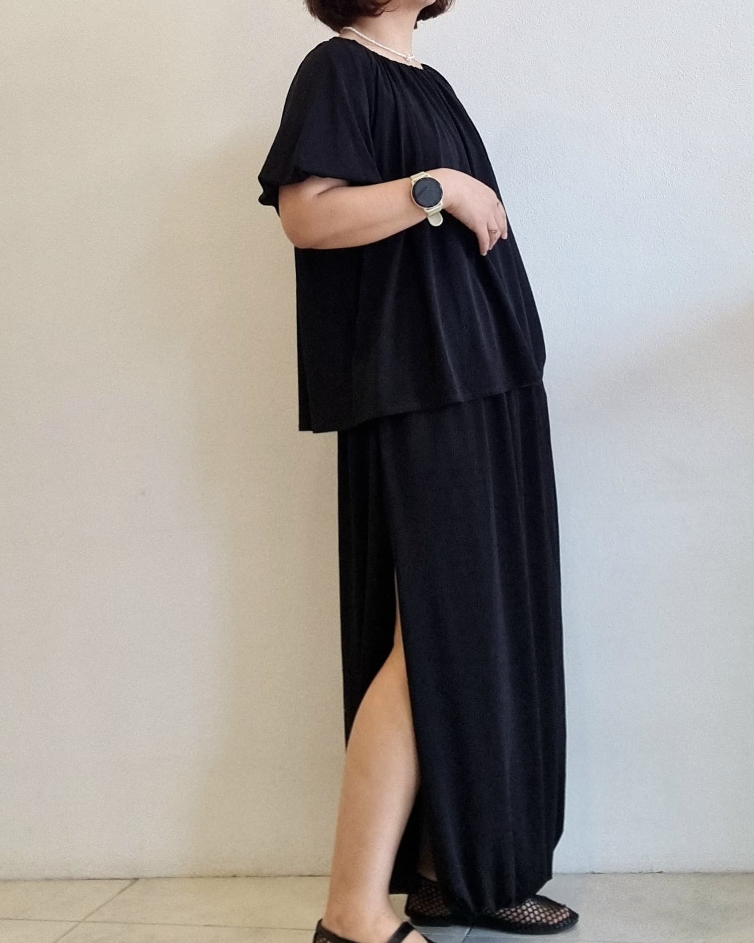 “Side view of a woman wearing the Seren Black Set with a relaxed top and slit maxi skirt.”