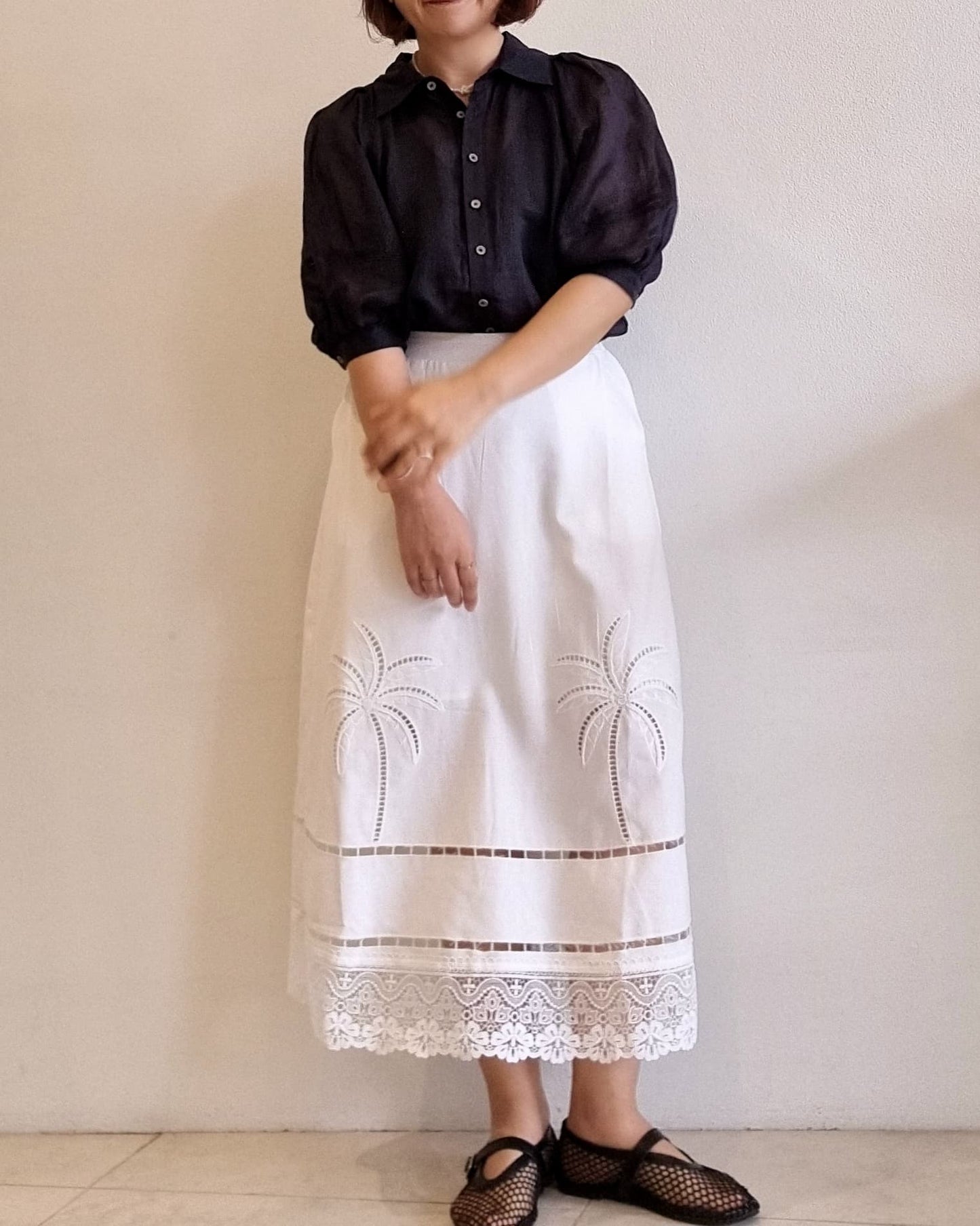 “Model wearing the Palmera Lace Skirt with palm embroidery and scalloped lace hem, styled with a black blouse.”