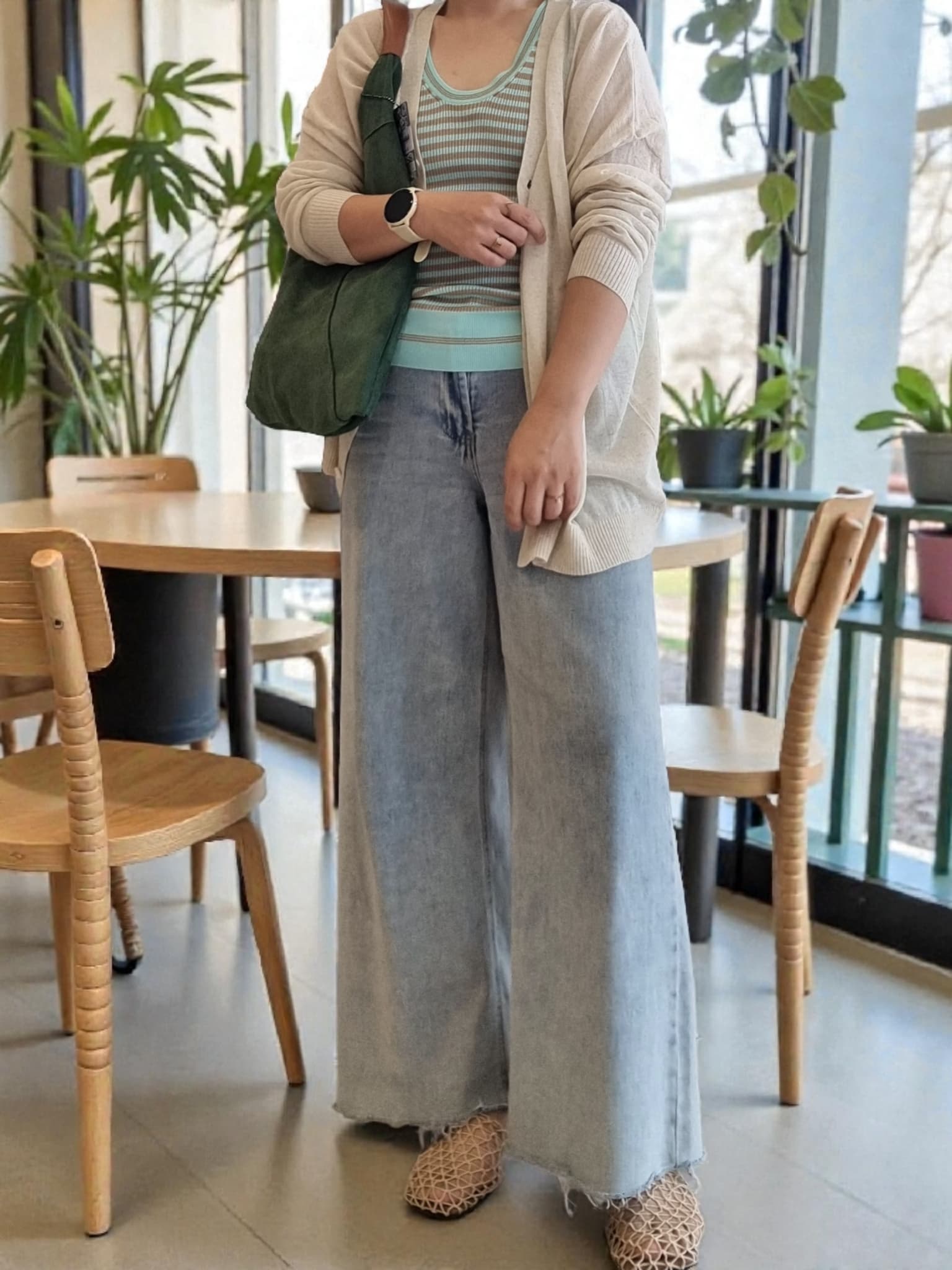 “Green Italian suede shoulder bag styled on a model in a cozy café setting, paired with wide-leg denim and a casual cardigan.”