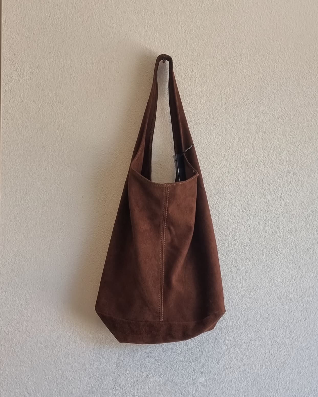 “Italian brown suede leather tote bag hanging against a beige textured wall”