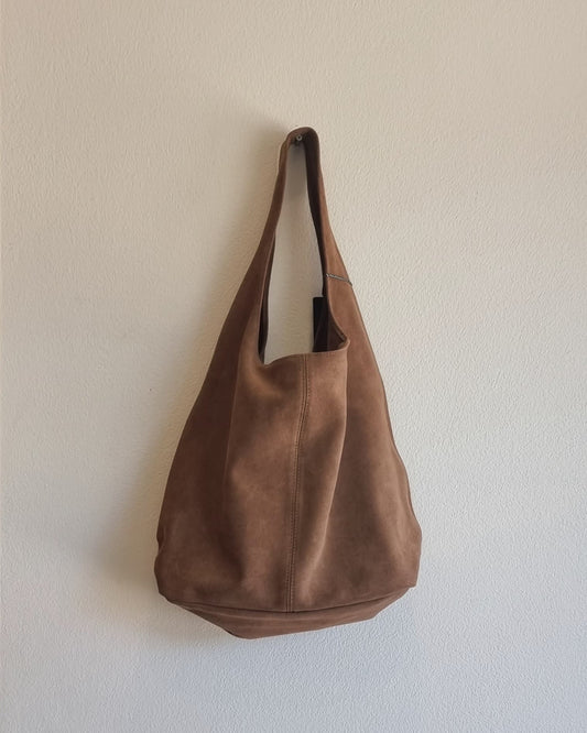 “Italian brown suede leather tote bag hanging against a beige textured wall”
