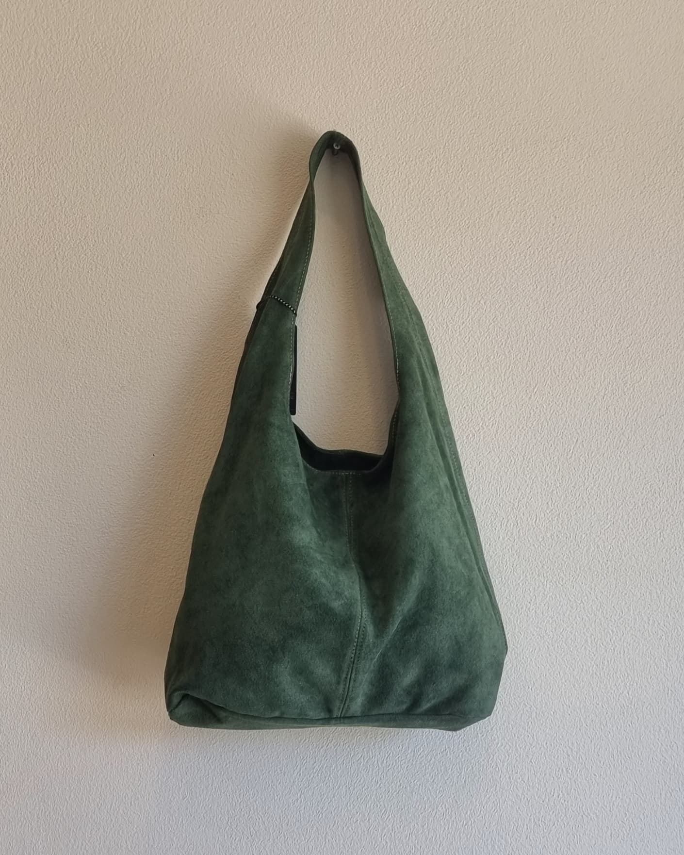 “Italian green suede leather tote bag hanging against a beige textured wall”