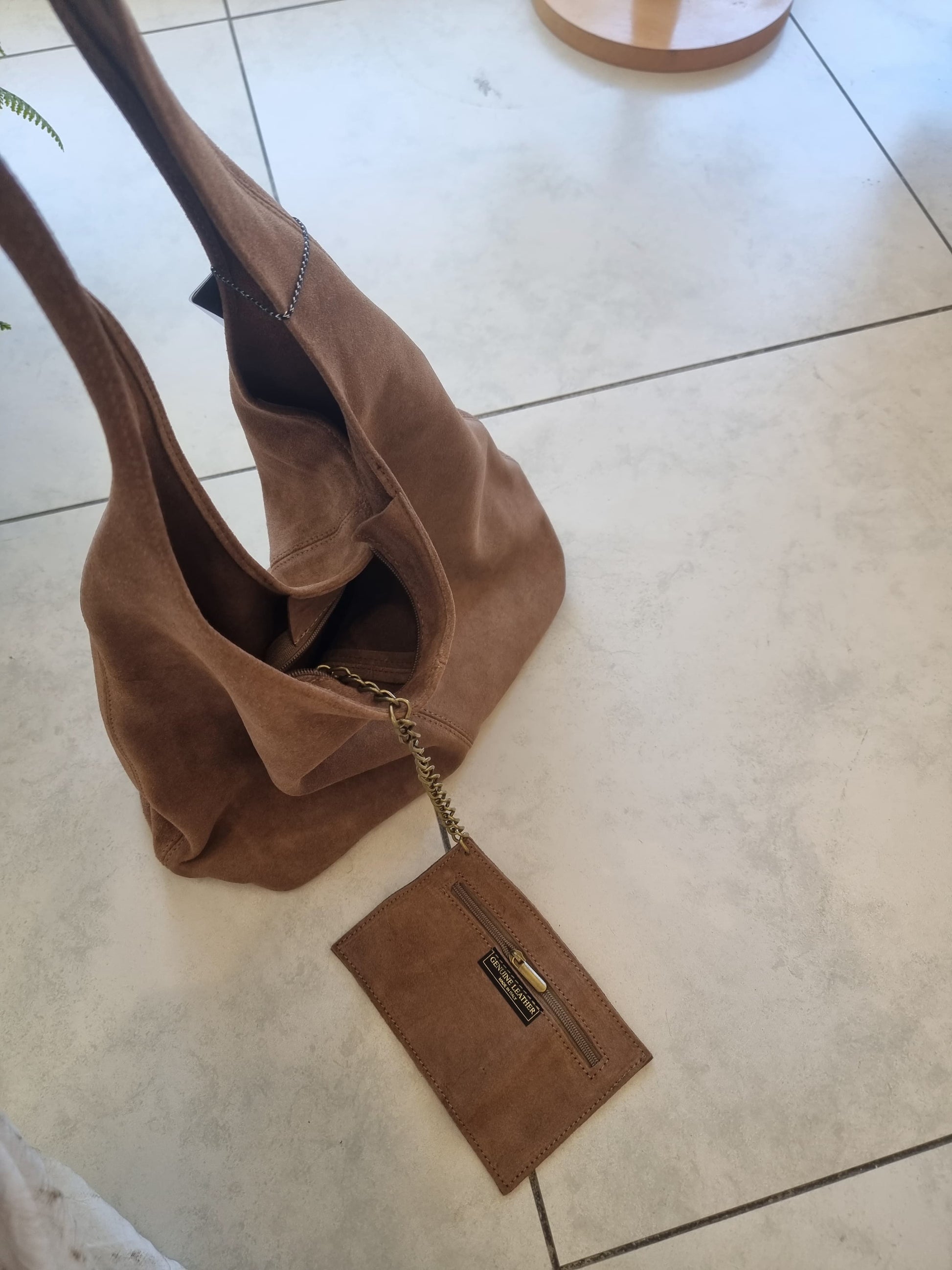 “Italian brown suede tote bag with a matching suede pouch, photographed from above on a light tile floor”