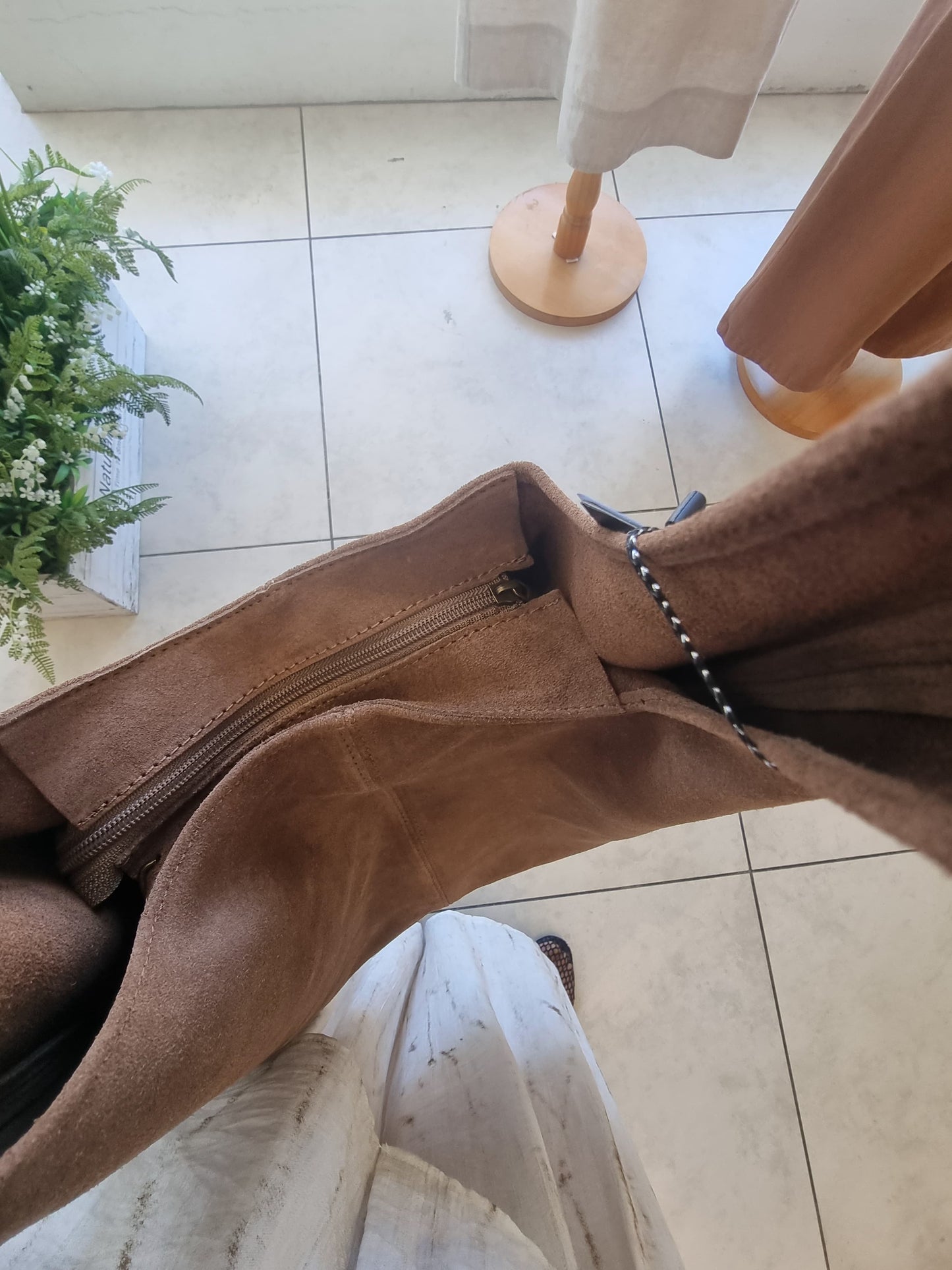 “Italian brown suede tote bag with zipper detail, photographed from above on a light tile floor”
