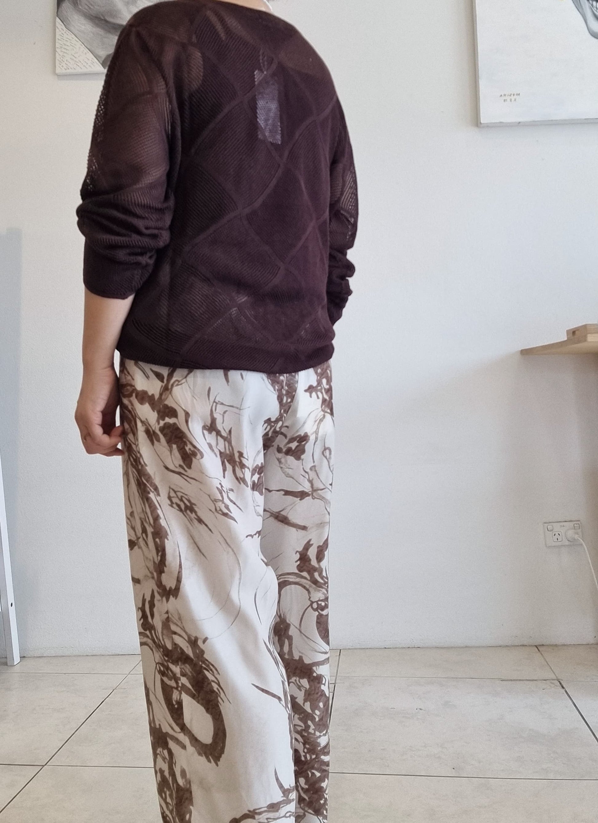 Back view of brown Tencel mesh knit long-sleeve top styled with beige abstract print wide-leg pants.