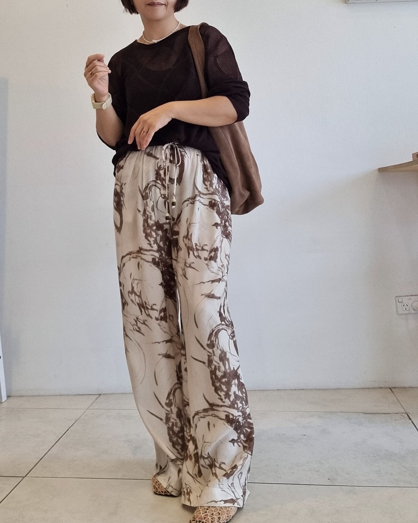 Model wearing elastic waist printed wide-leg pants with a full-length relaxed fit in a minimal indoor setting.