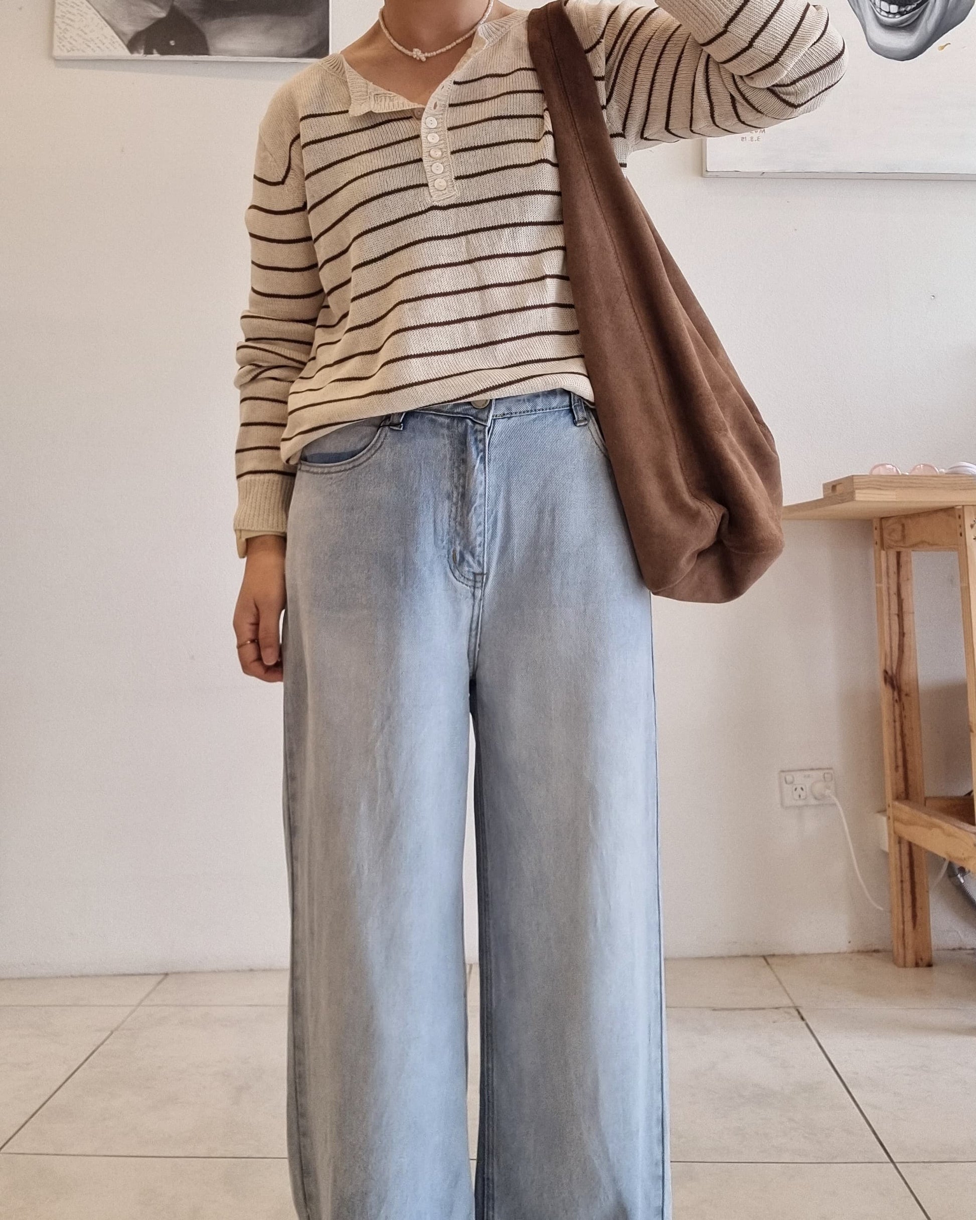 “Model wearing a beige cotton summer knit top with brown stripes, styled with wide-leg light blue denim jeans and a brown shoulder bag.”