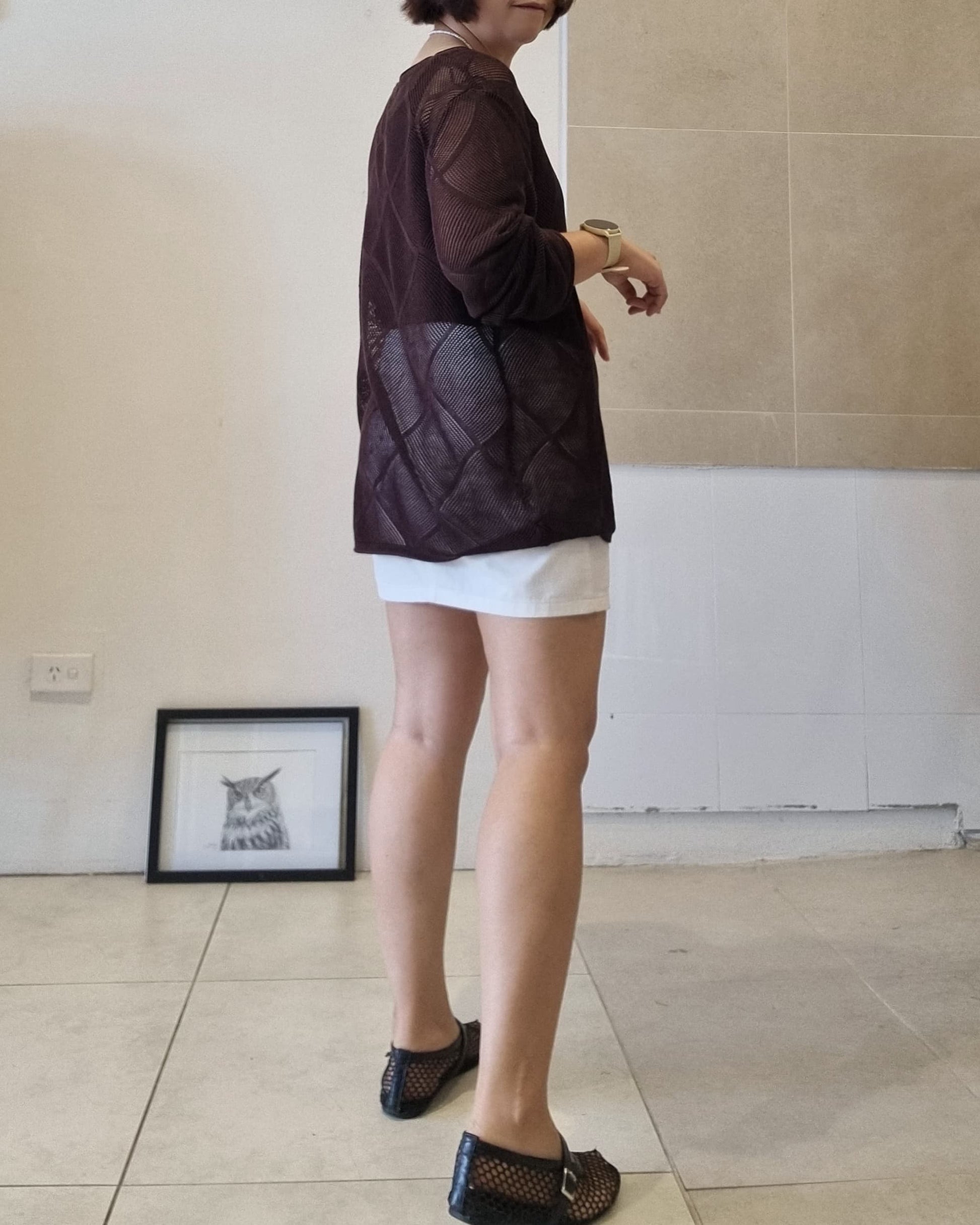 Dark brown sheer knit long-sleeve top styled over white shorts, back view