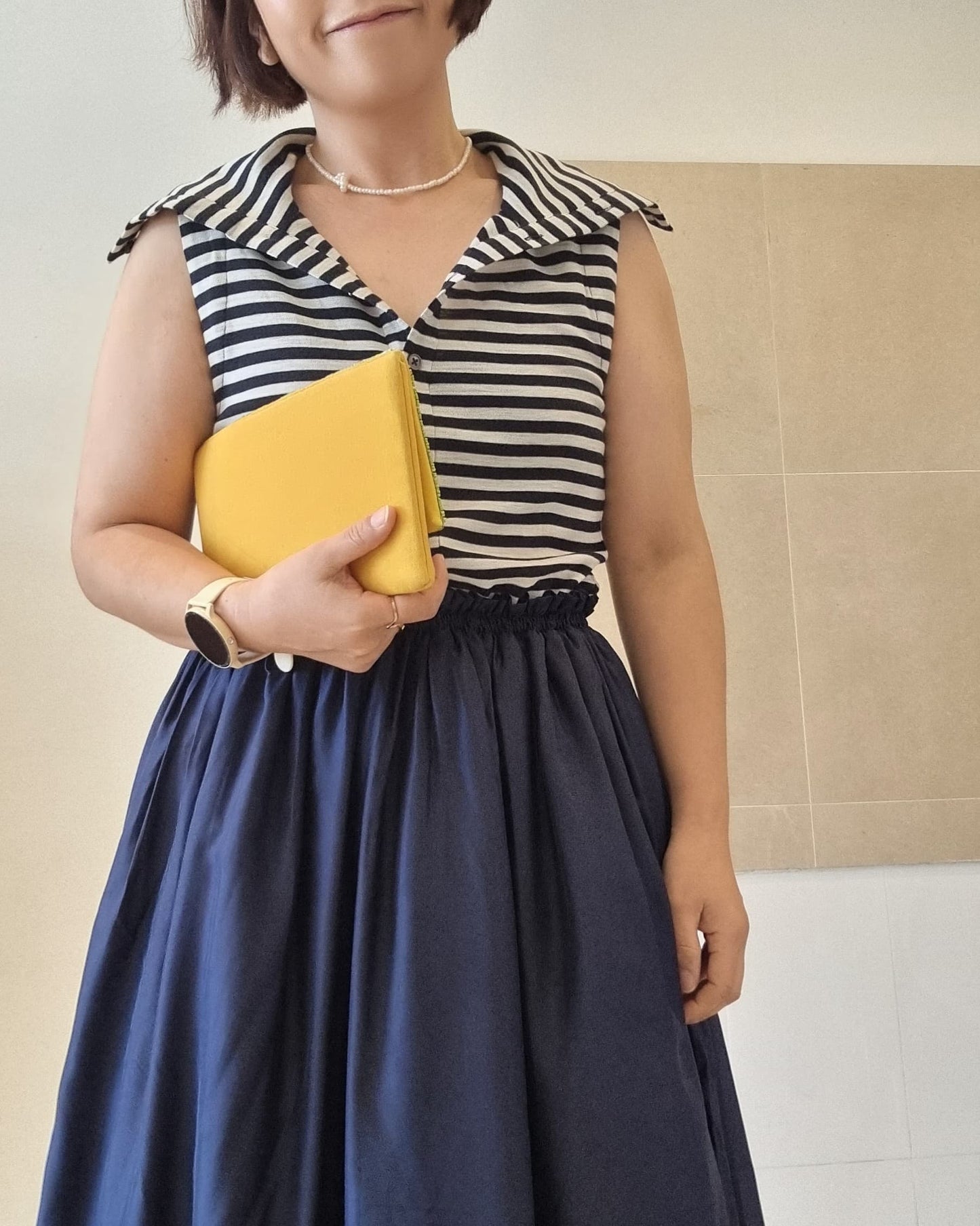 Model wearing a navy silk midi skirt dress with elastic waist, styled with a striped sleeveless top and yellow clutch