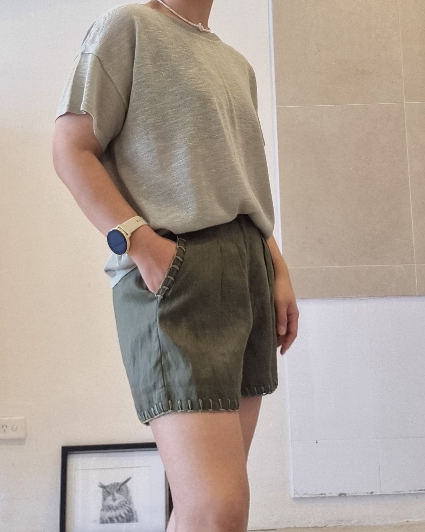 Side view of soft green viscose knit top worn by model, relaxed fit, styled with dark green shorts