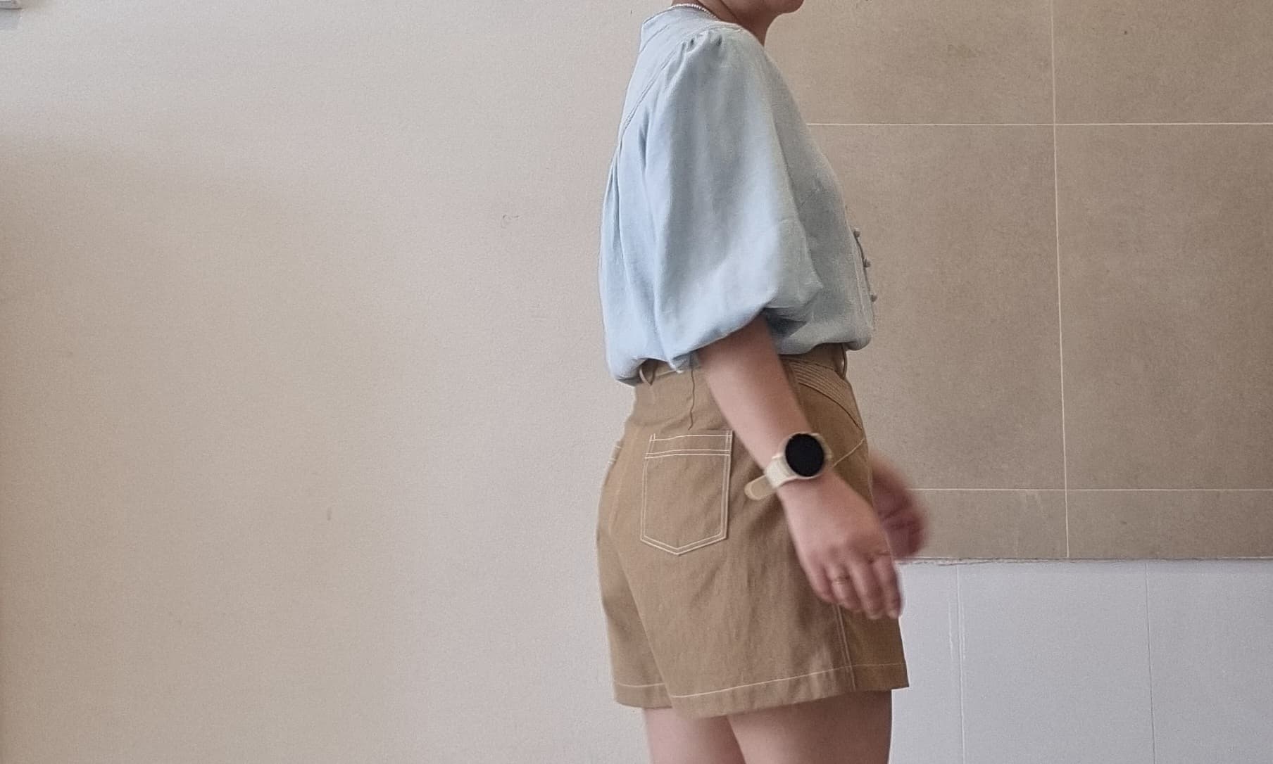 Side back view of model wearing Selene light blue Tencel blouse with high-waisted brown shorts