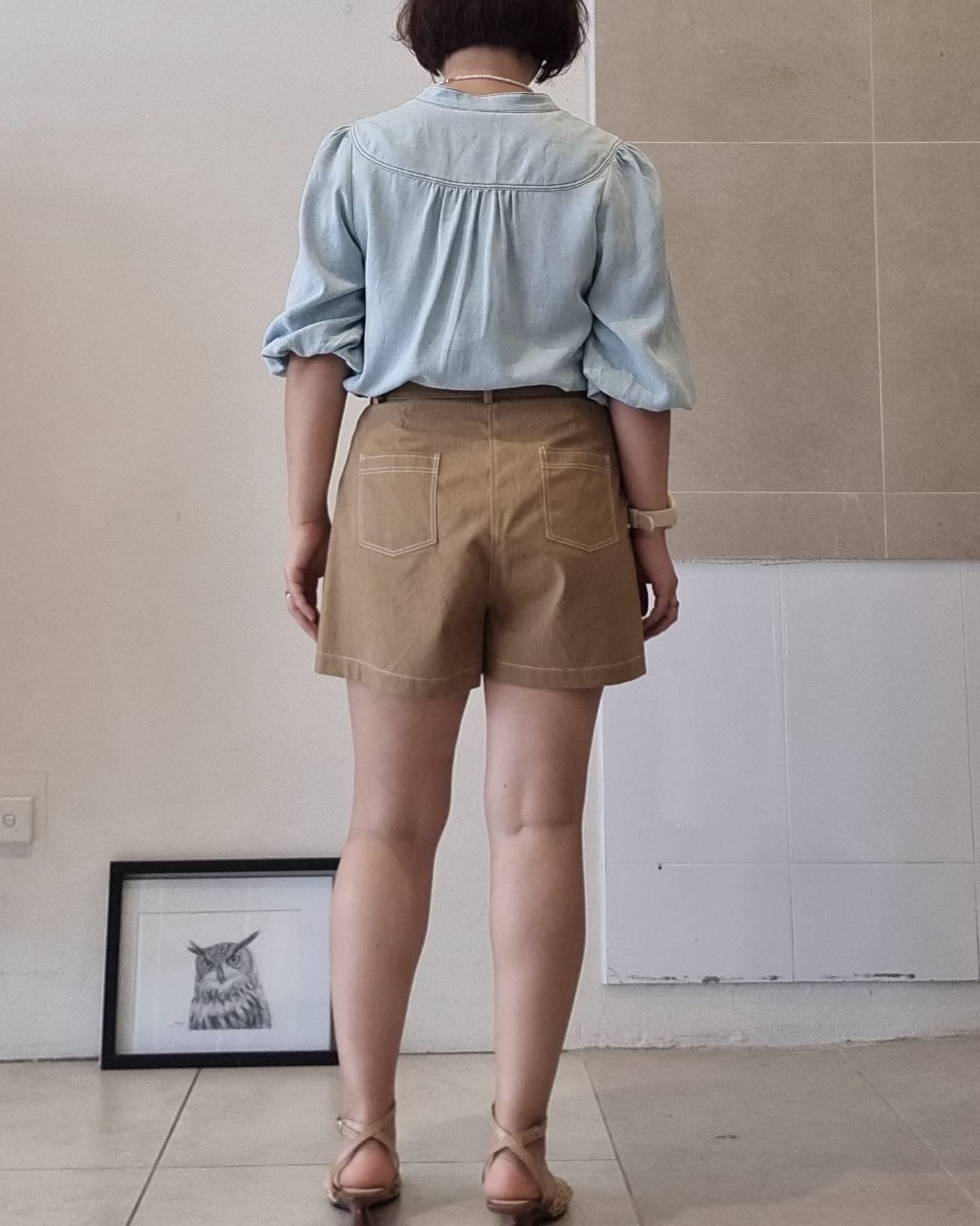 Back view of model wearing Selene light blue Tencel blouse with high-waisted brown shorts