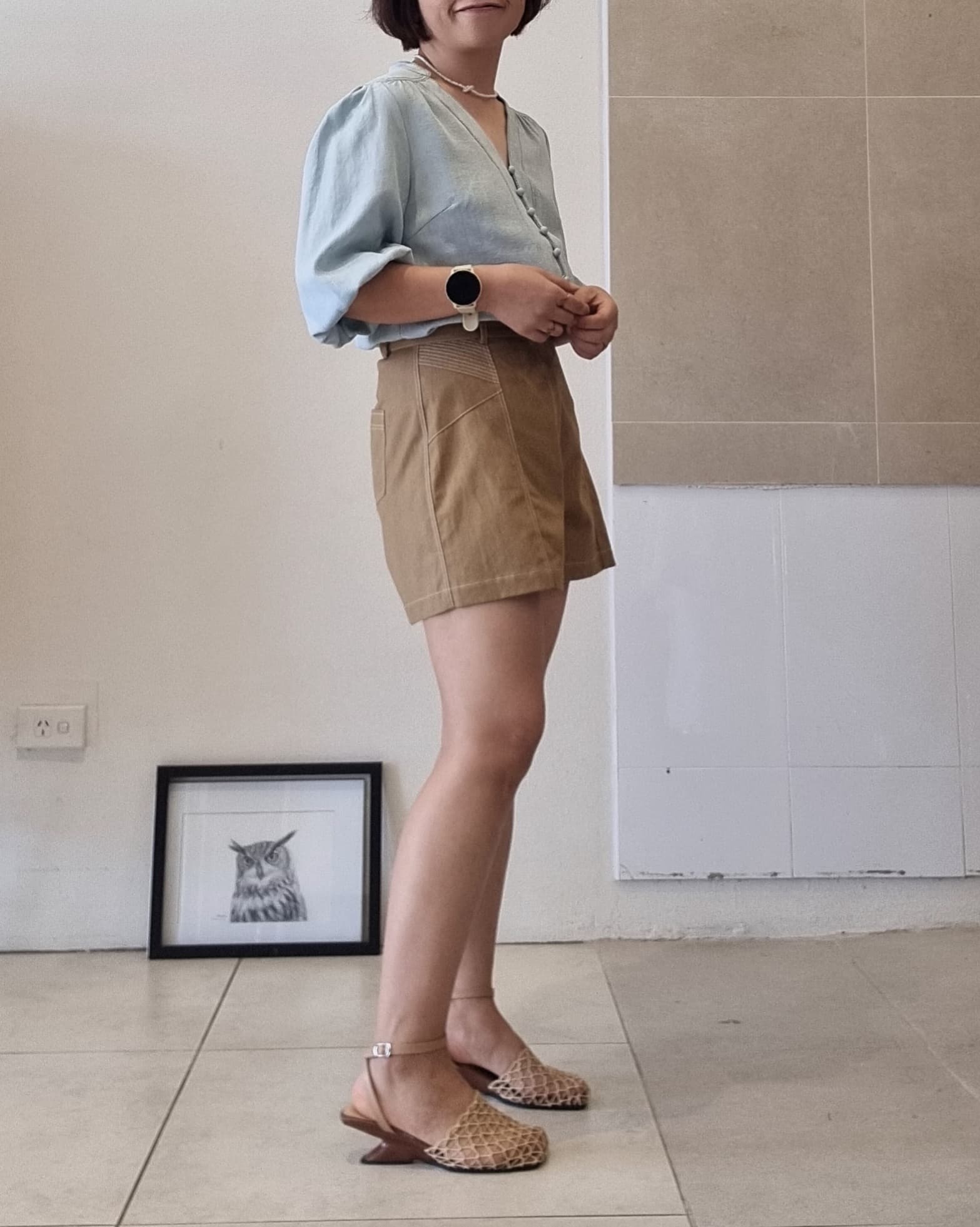 Side view of model wearing Selene light blue Tencel blouse with high-waisted brown shorts