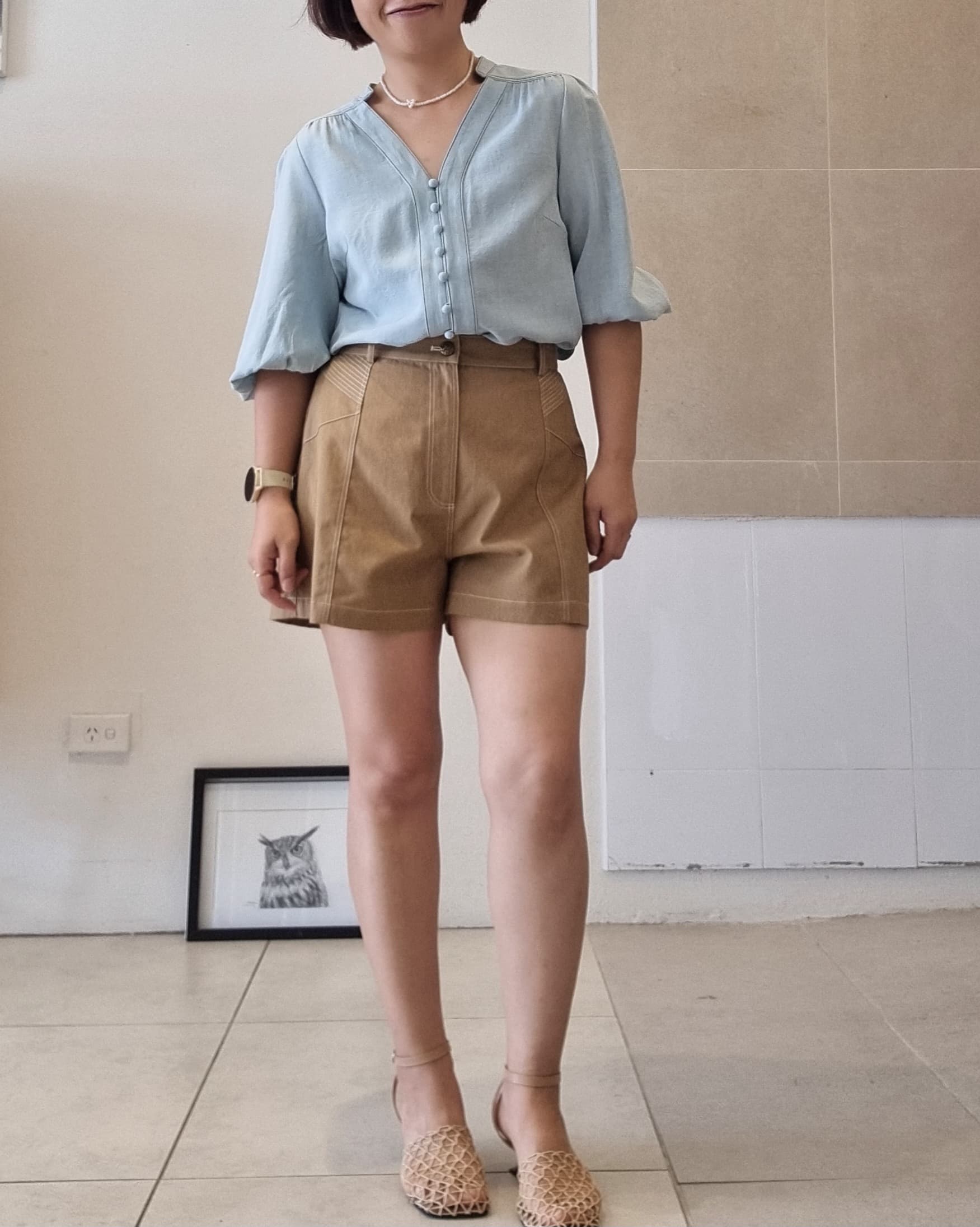 Model wearing Selene light blue Tencel blouse styled with high-waisted brown shorts