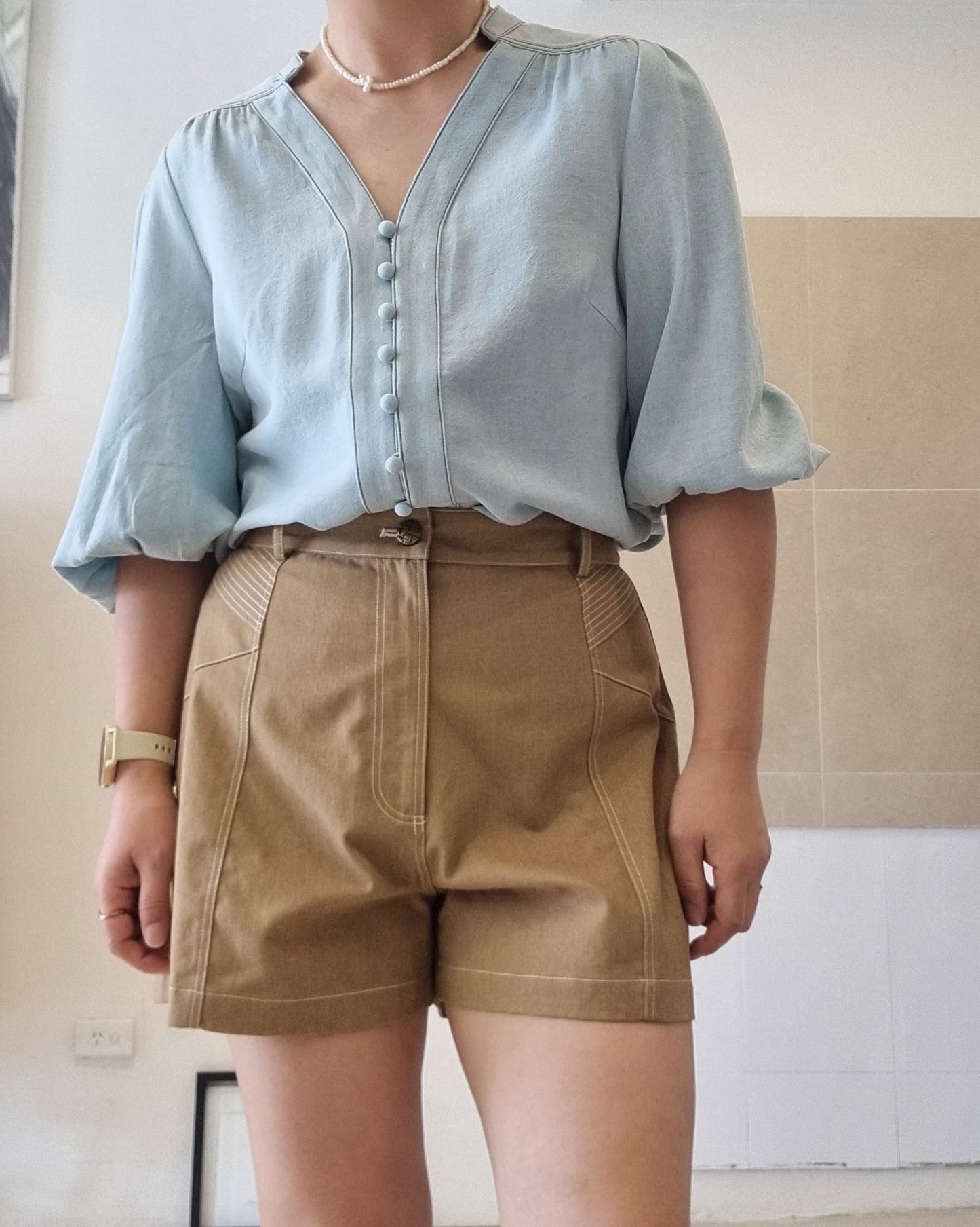 Model wearing Selene light blue Tencel blouse with high-waisted brown shorts