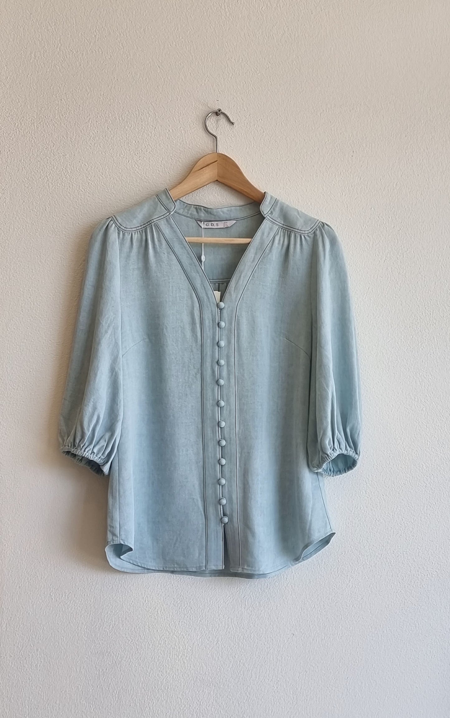 Selene light blue Tencel blouse hanging on a wooden hanger