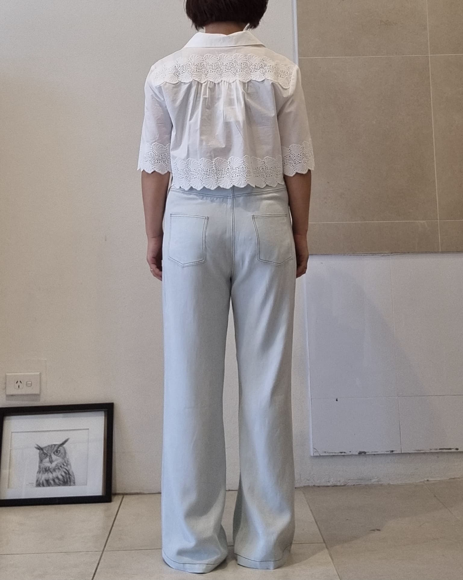 White cotton eyelet lace blouse with scalloped hem and back yoke detail, back view on model