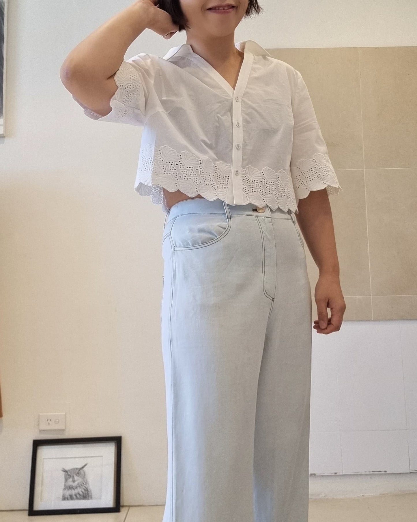 White cotton eyelet lace blouse with scalloped hem, side view styling with light blue high-waist pants