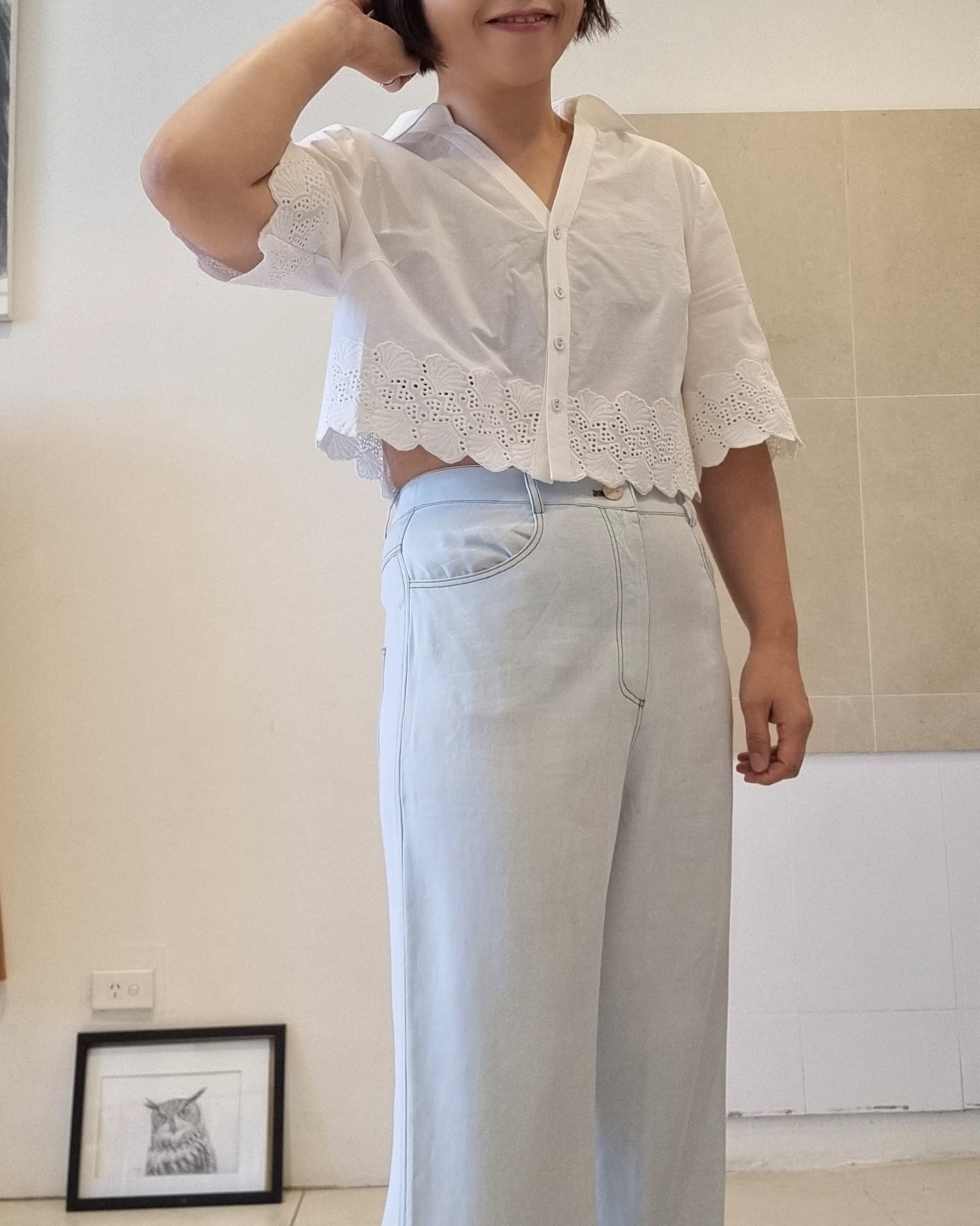 White cotton eyelet lace blouse with scalloped hem, side view styling with light blue high-waist pants