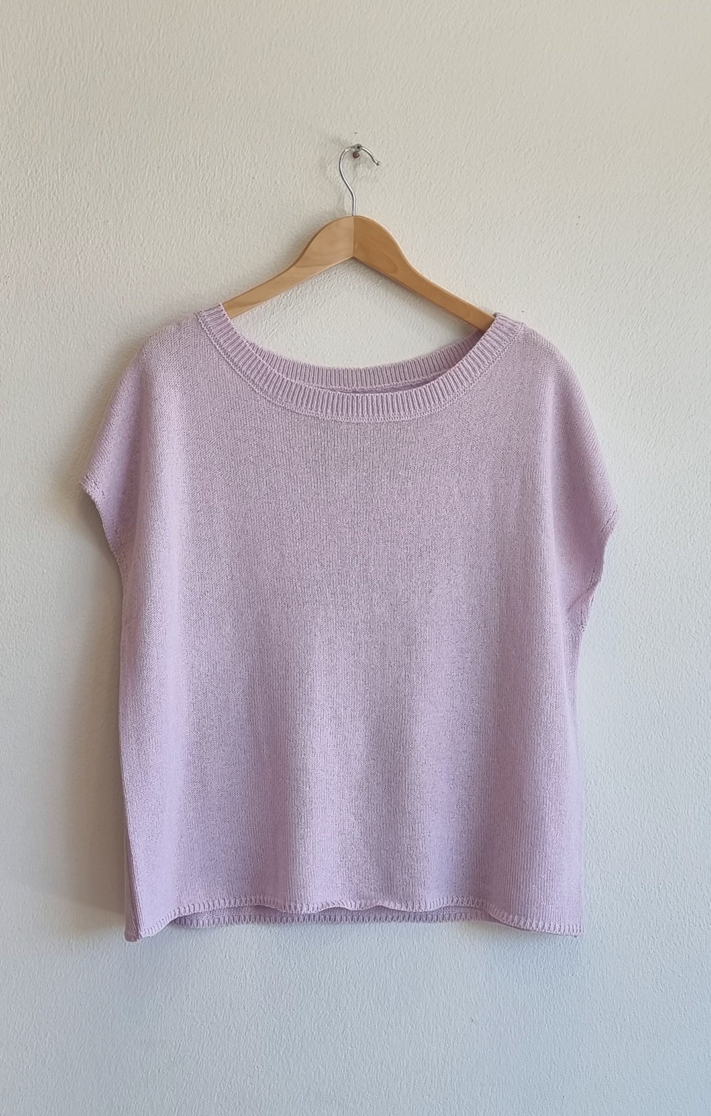 Light purple knit short-sleeve top hanging on a wooden hanger against a white wall, featuring a relaxed fit and soft textured fabric.