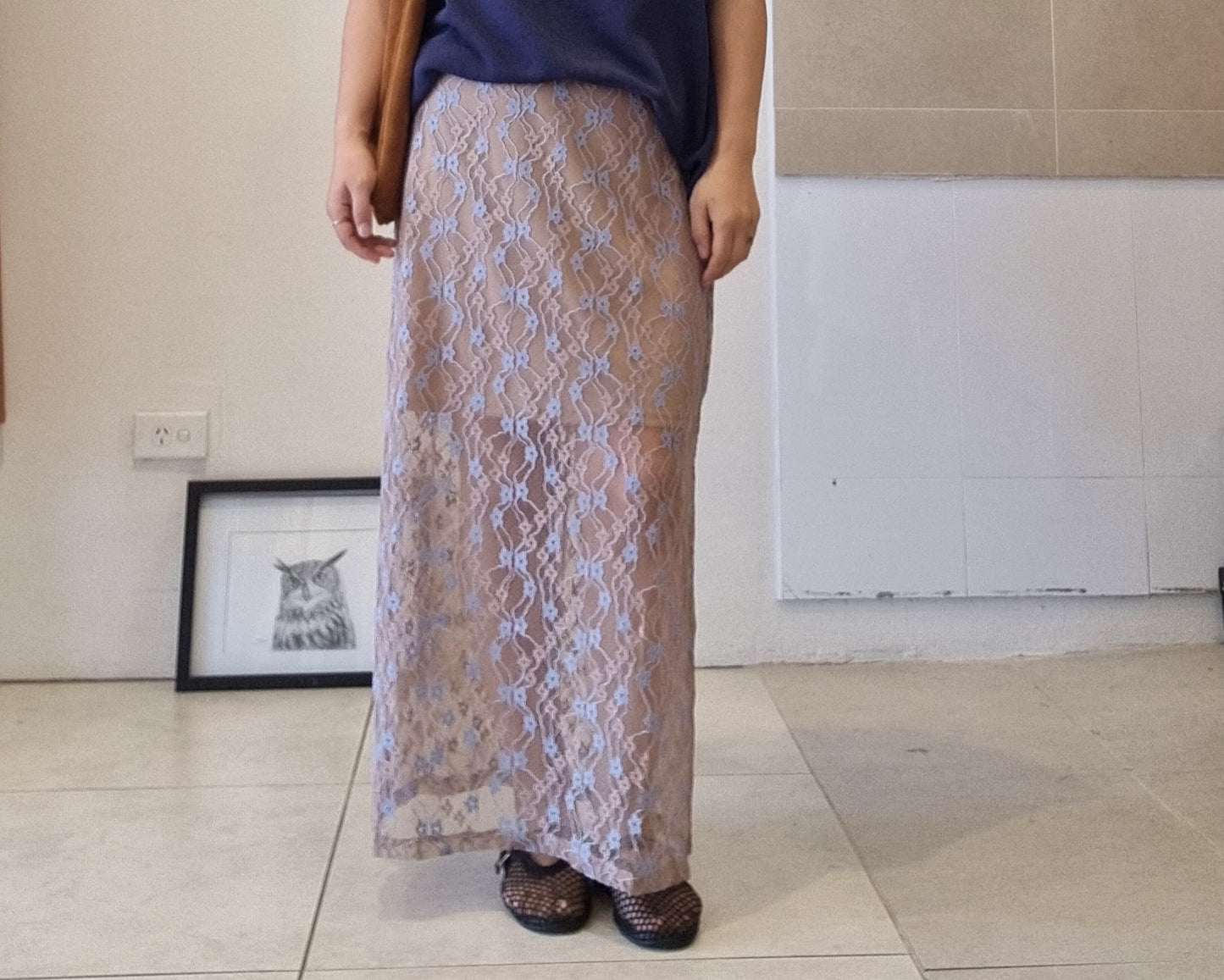 Model wearing a sheer lace maxi skirt with knee-length lining and elastic waistband, styled casually indoors.