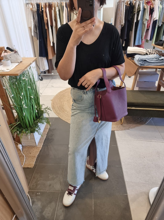 Woman wearing a burgundy genuine leather bucket tote bag with gold buckle in a boutique setting.