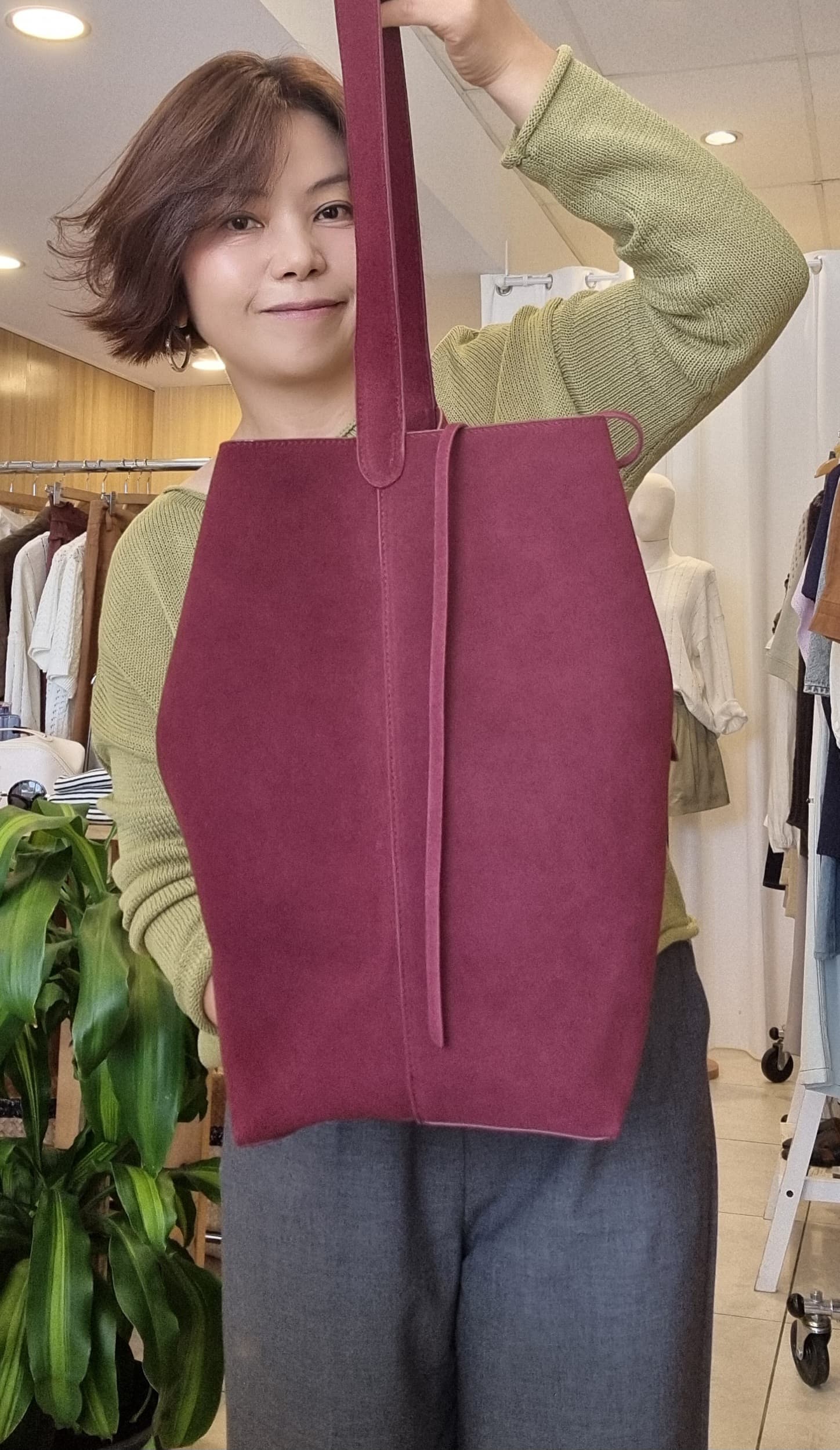 Model wearing a green top and knit, holding the Burgundy Suede Tote, front view