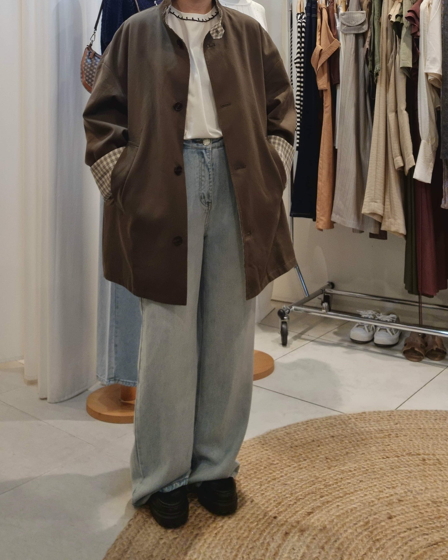 Model wearing khaki reversible trench coat with blue jeans, front view