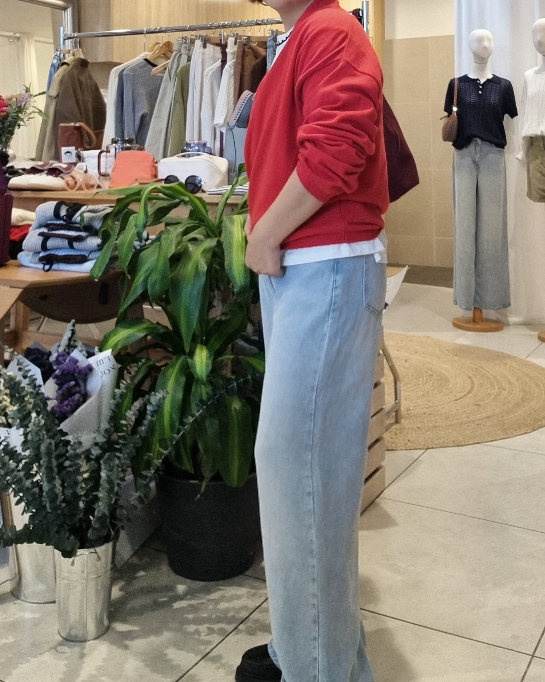 Side view of model wearing red wrap knit with blue jeans, draped silhouette