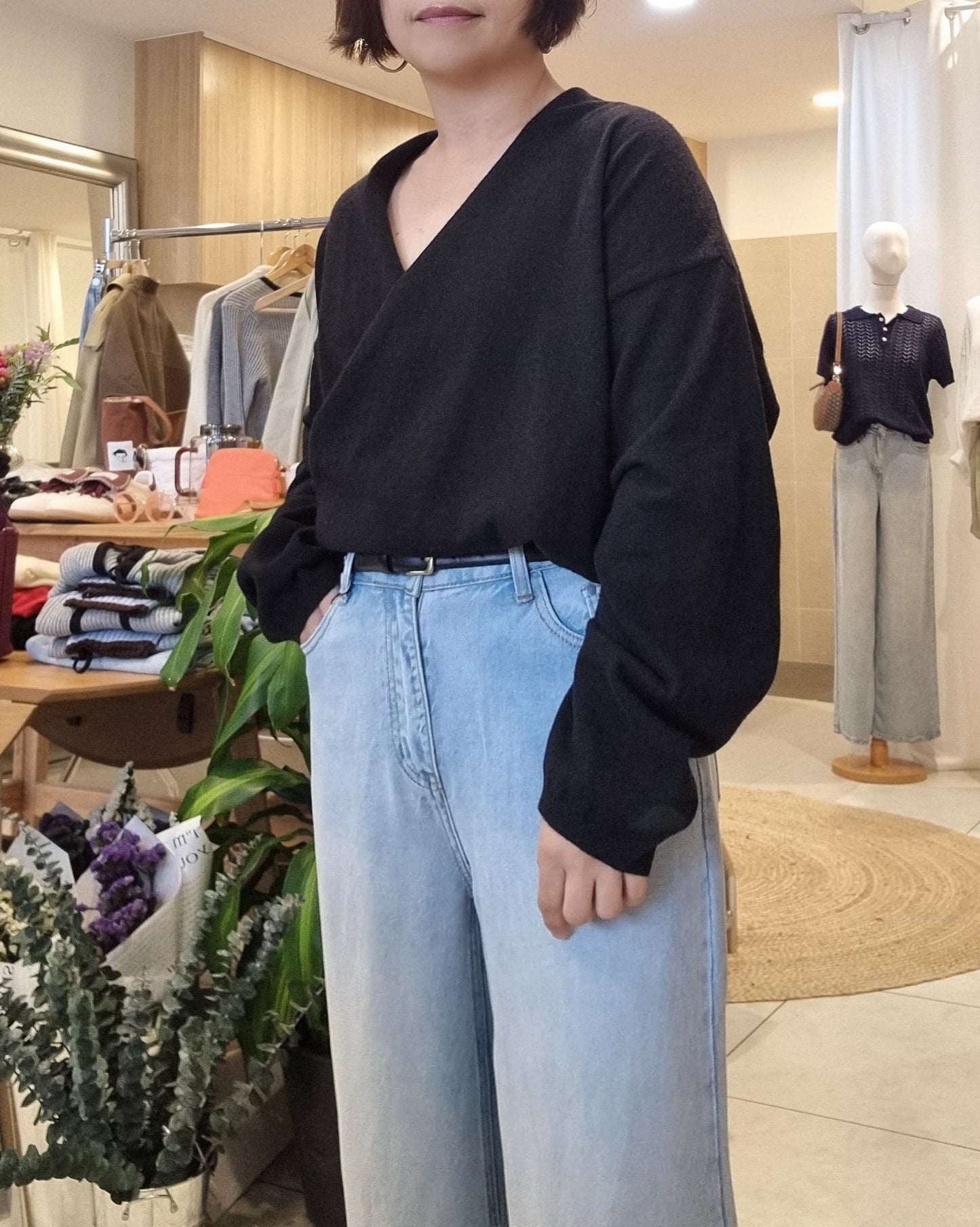 Side view of model wearing Black wrap knit with blue jeans, draped silhouette