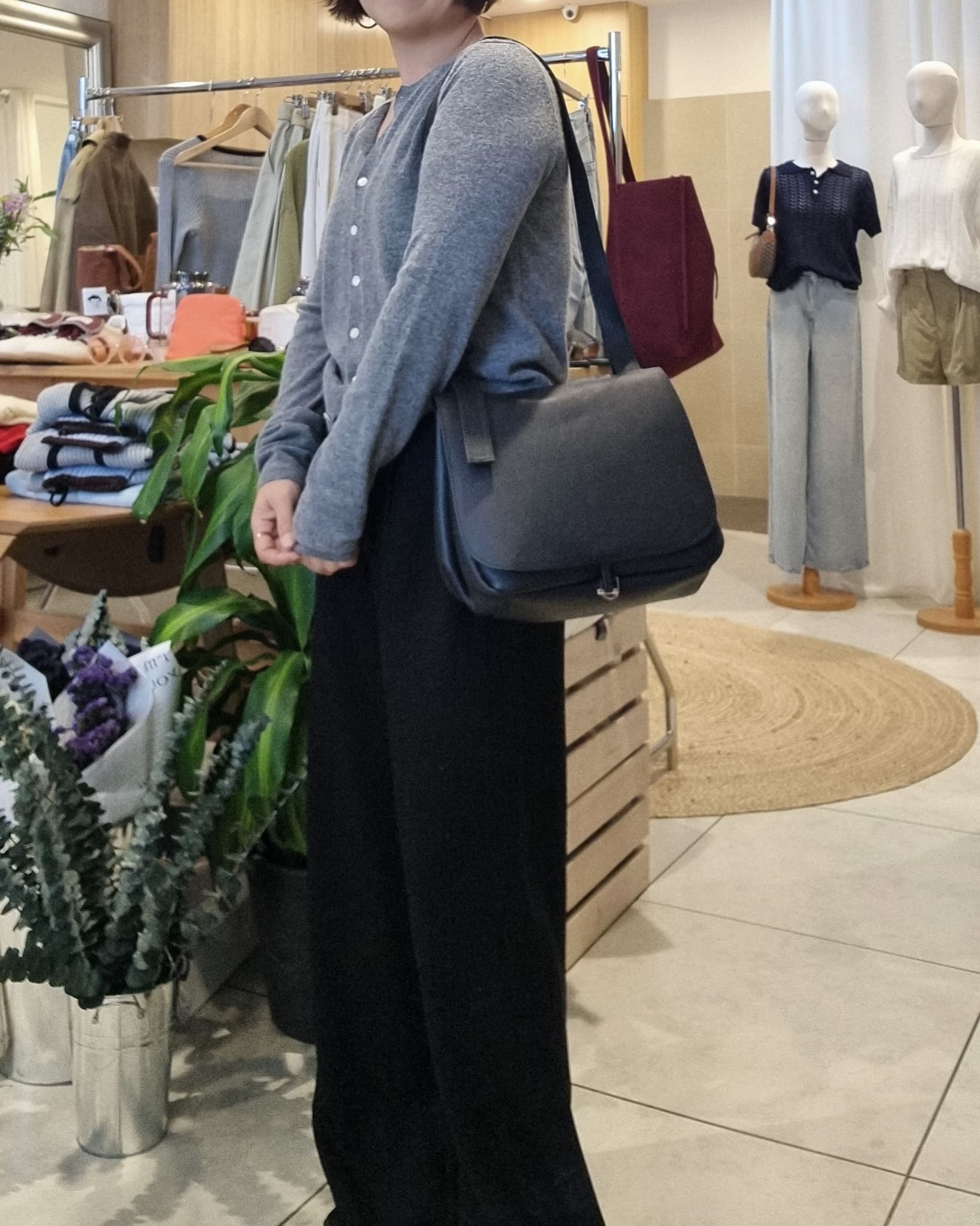 Model wearing black leather crossbody bag with grey cardigan and black pants