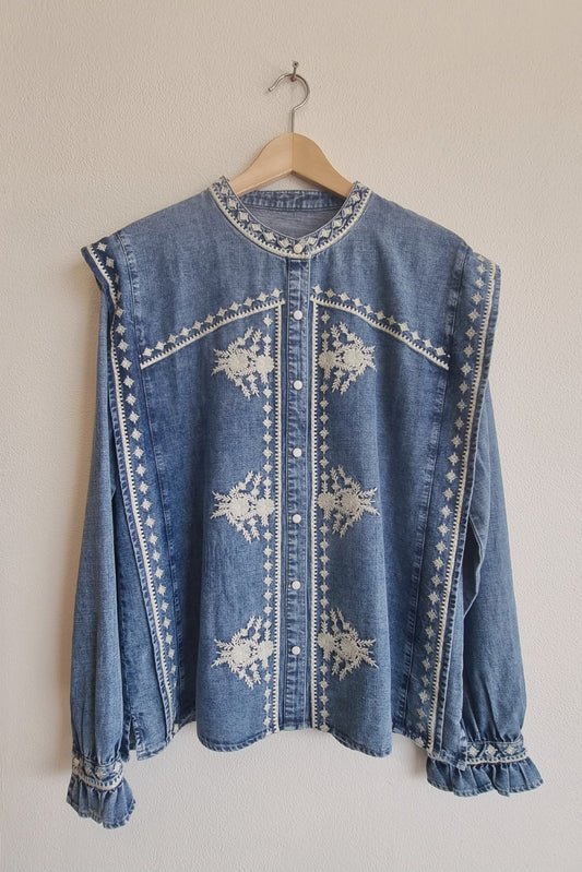 Front view of blue embroidered cotton denim blouse with floral detailing and button closure