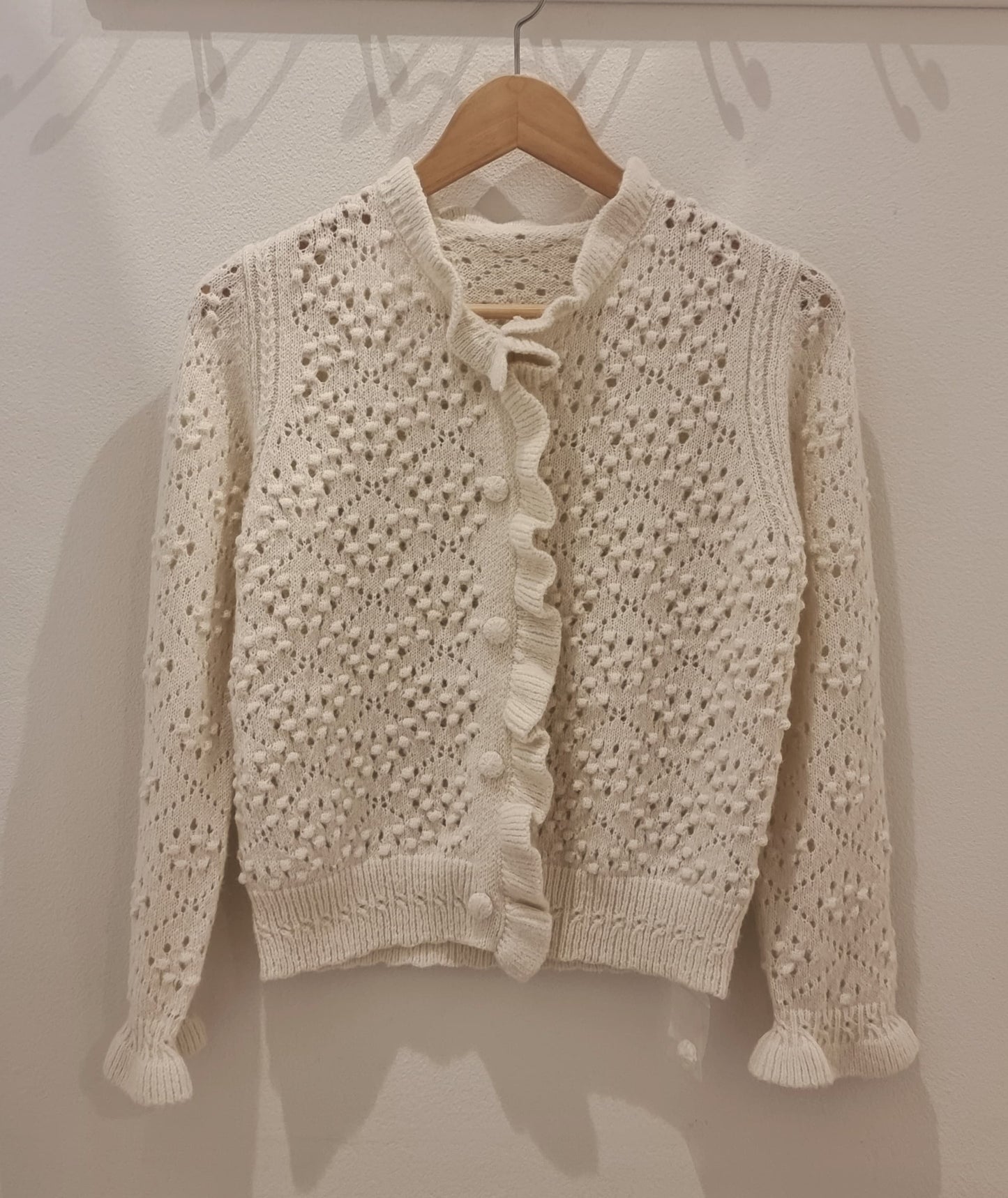 Front view of cream alpaca blend ruffle knit cardigan with textured detailing