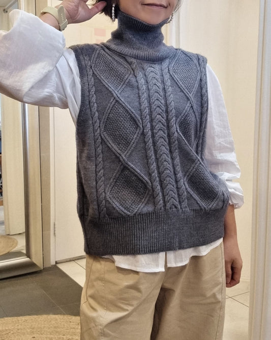 Model wearing a grey cable knit vest layered over a white shirt