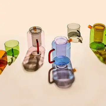 Three colorful Cha Pots in pink, blue, and green with matching glass cups arranged on a beige surface, creating soft shadows