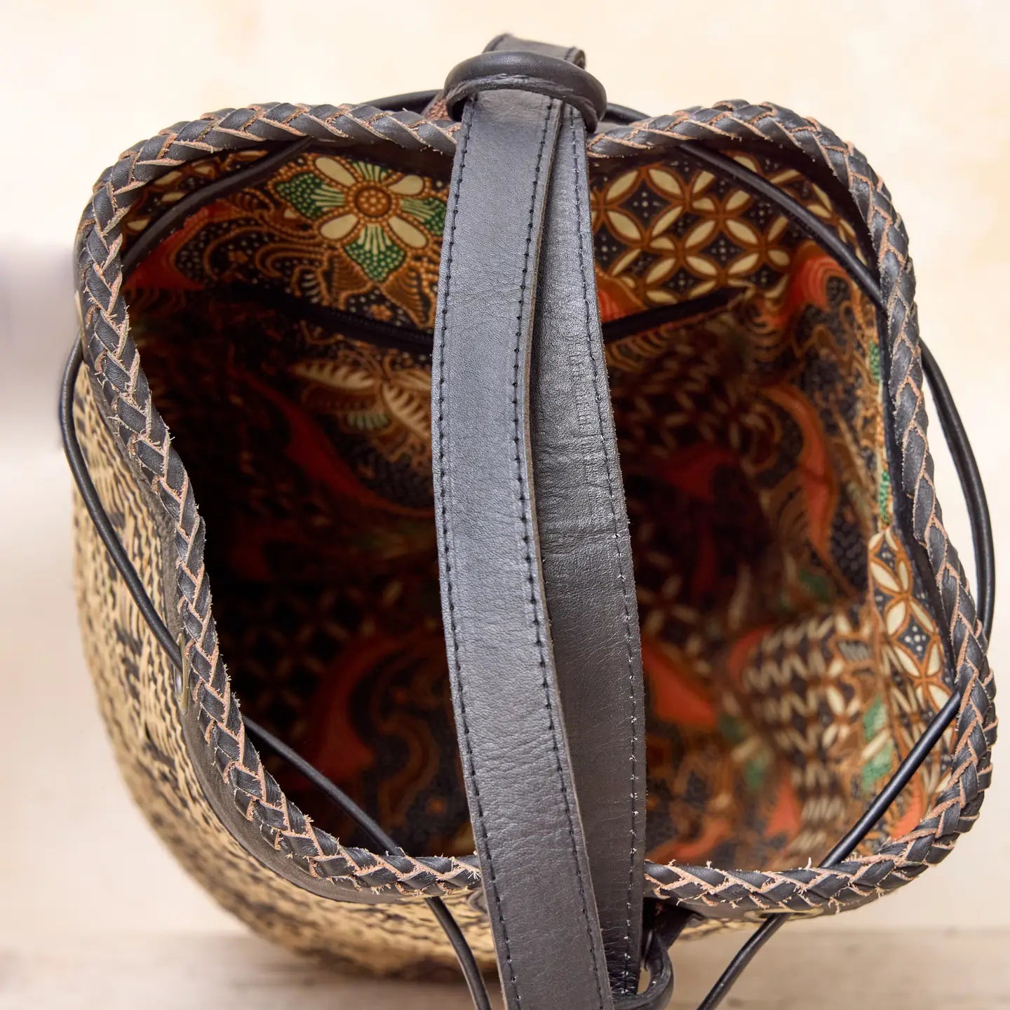 “Top view of a handwoven Borneo rattan bag showing the batik-print interior lining and dark leather strap.”
