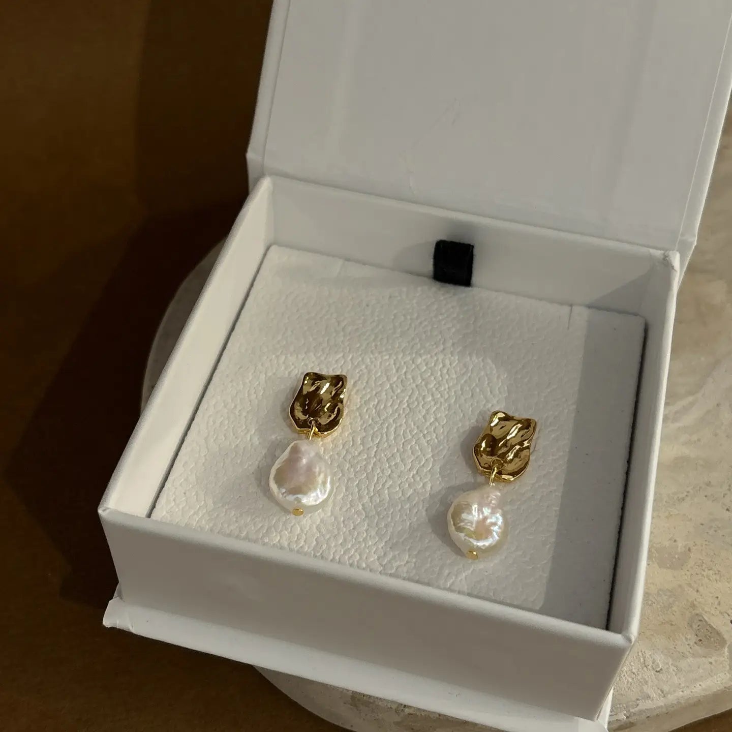 Pair of gold-plated textured studs featuring round baroque pearls, photographed in soft natural lighting.