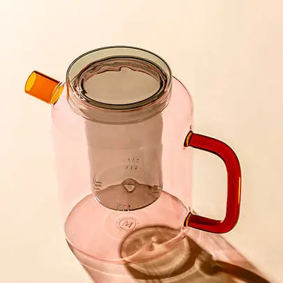 Pink glass Cha Pot with a red handle and yellow spout on a beige background