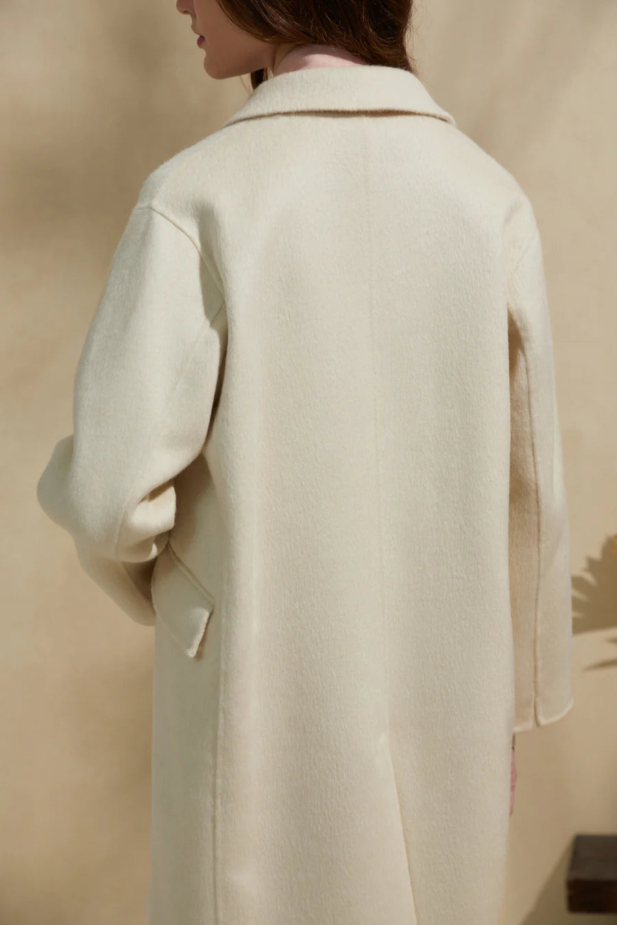 Back view of cream merino wool coat showing clean tailoring and relaxed silhouette