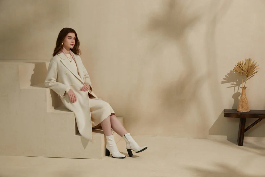 Woman seated wearing a cream wool coat in a soft neutral studio setting