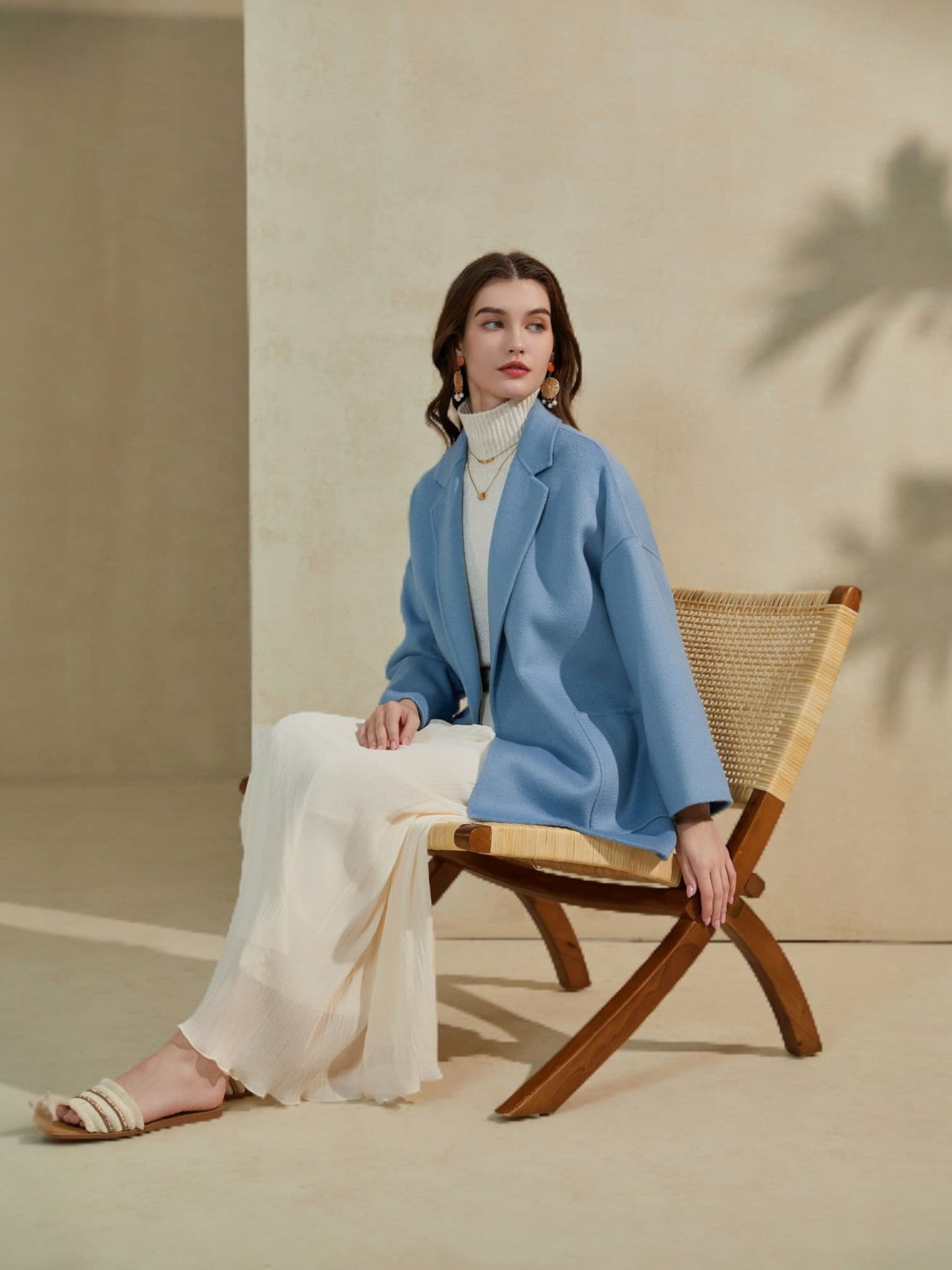 “Light blue oversized blazer paired with an ivory skirt, styled while seated on a woven wooden chair in a minimal neutral setting.”