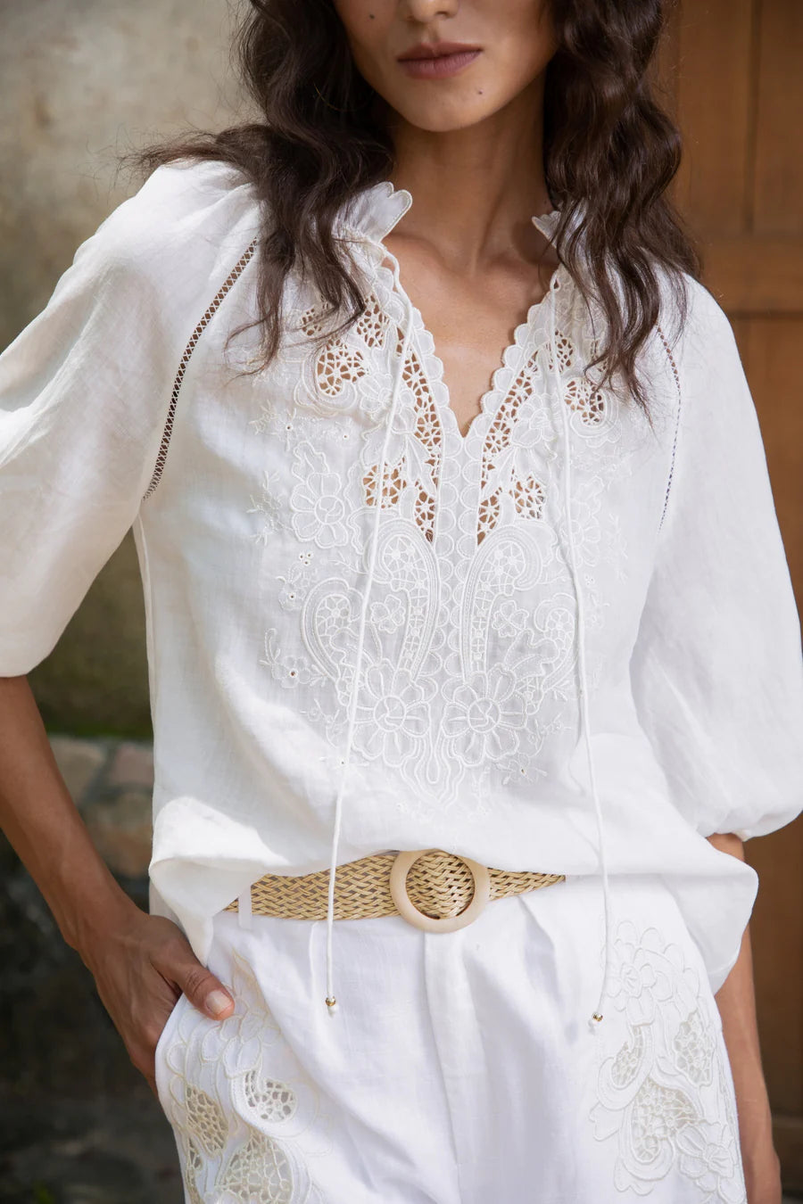 "White embroidered blouse with floral lace details and V-neckline worn with white shorts."