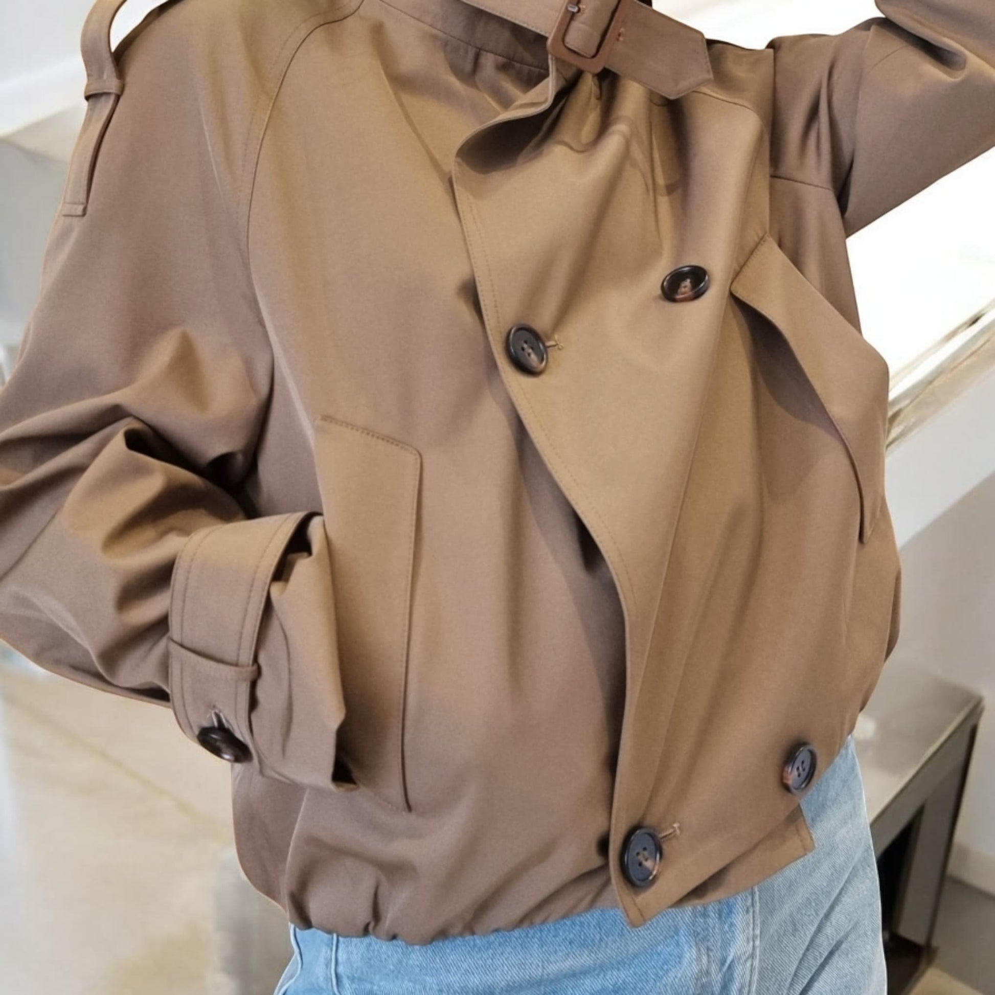 “Close-up view of a beige cropped trench coat with double-breasted buttons and structured sleeves.”