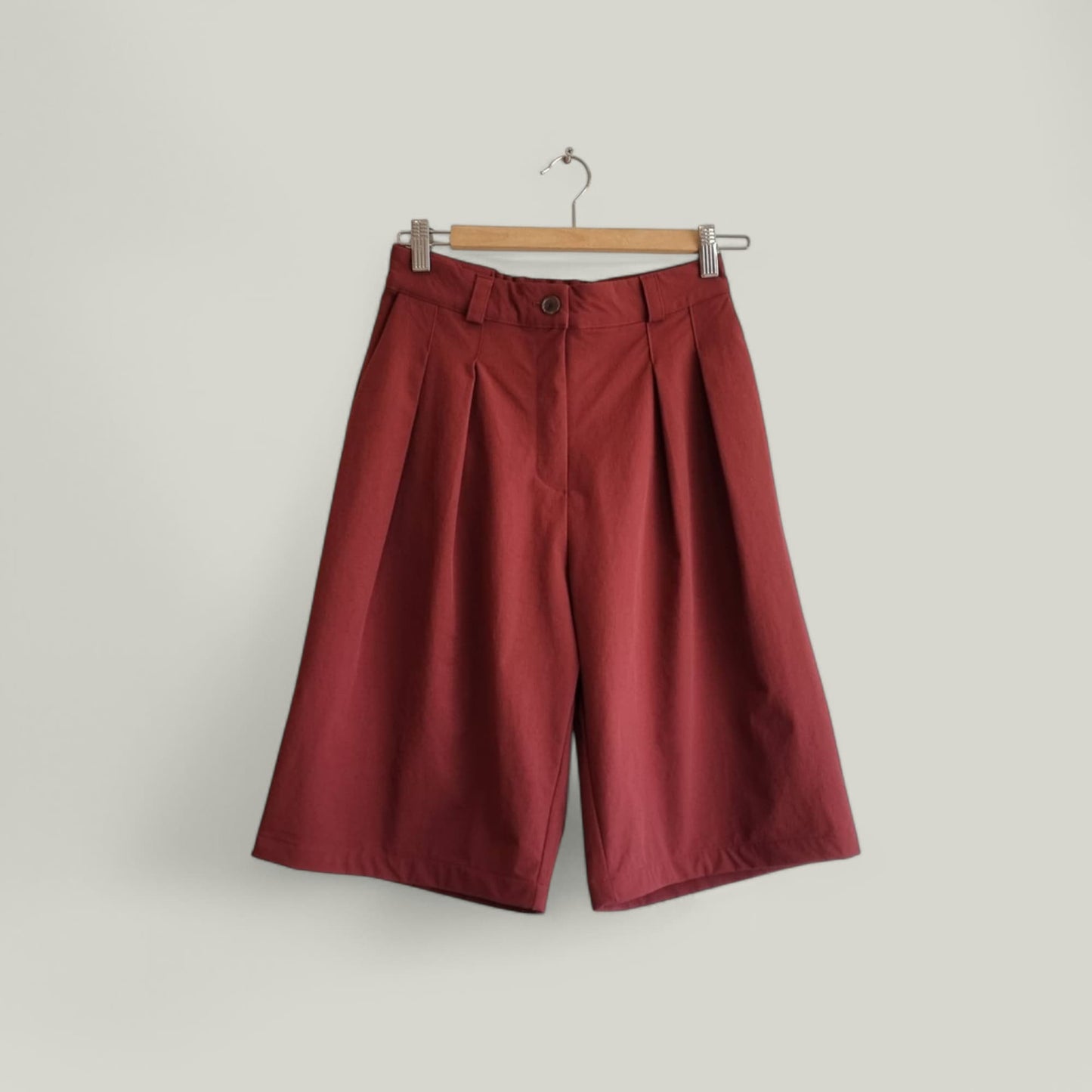 Burgundy wide-leg pants hanging on a wooden hanger – front view