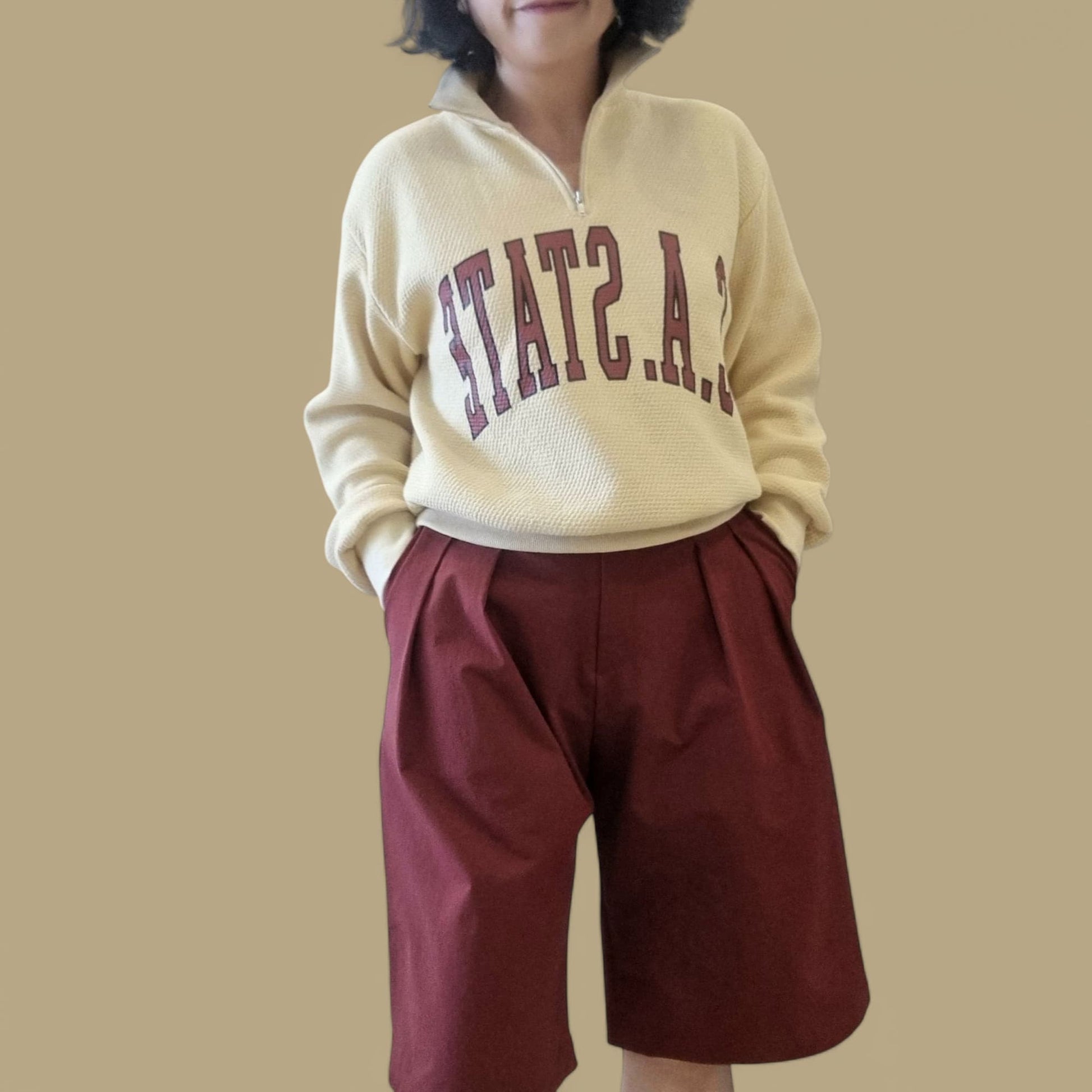 Model wearing beige zip-up sweatshirt with burgundy shorts – front view