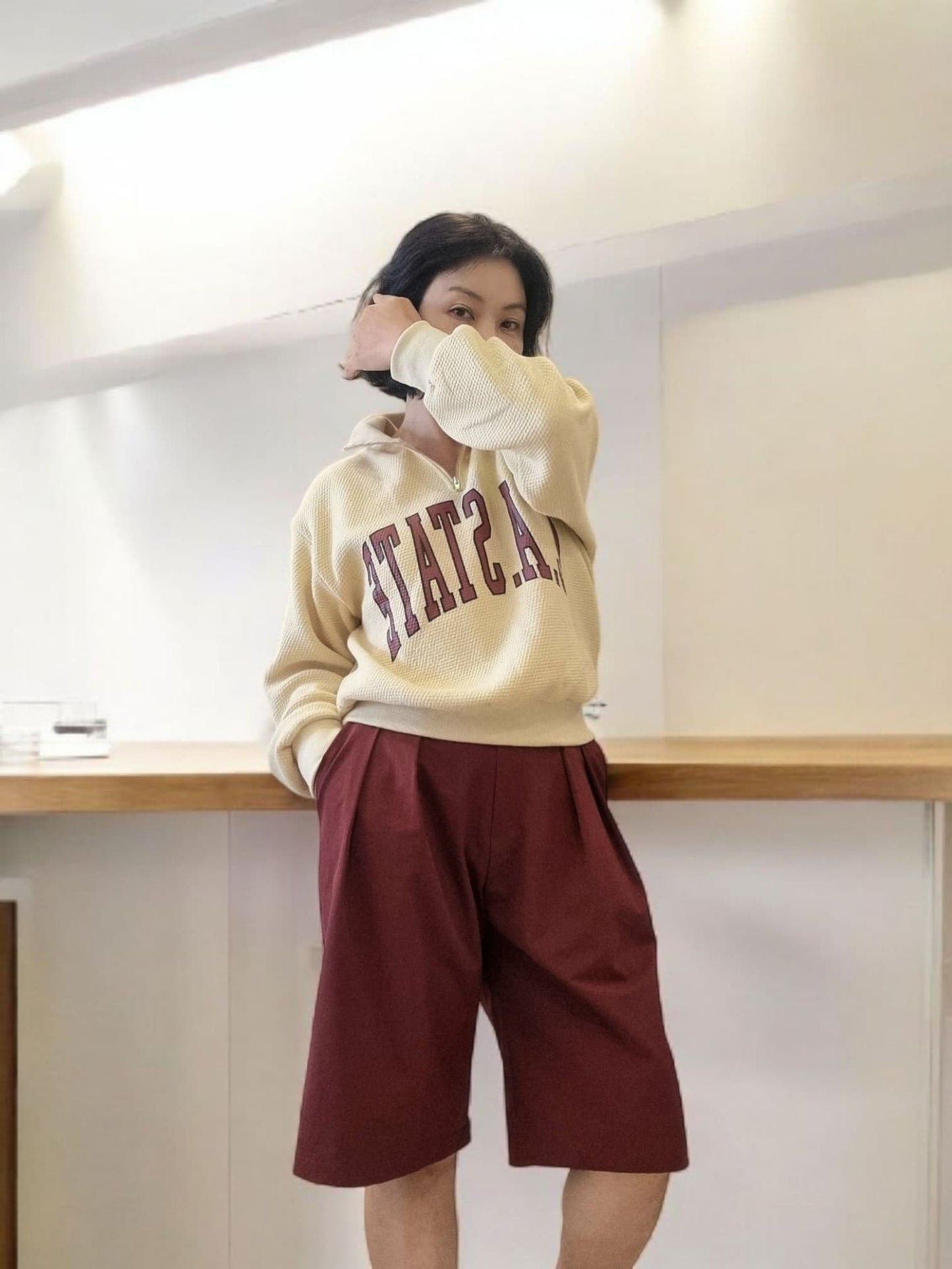 Model adjusting burgundy pants waistband – close-up